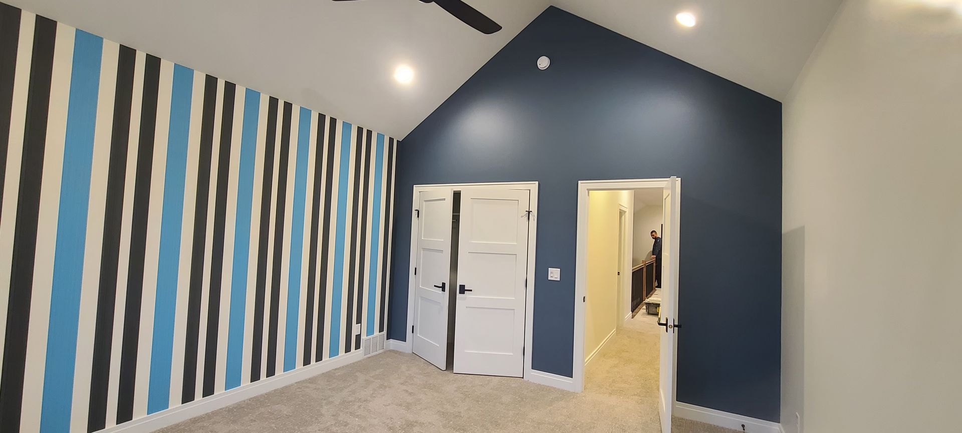 Room with blue and black striped wall, blue accent wall, white doors, and light-colored carpet.