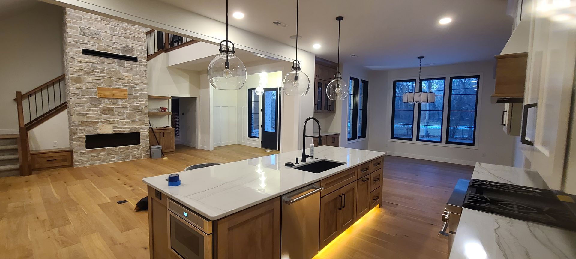 Spacious open-concept kitchen with large island, stone fireplace, and light wood floors.