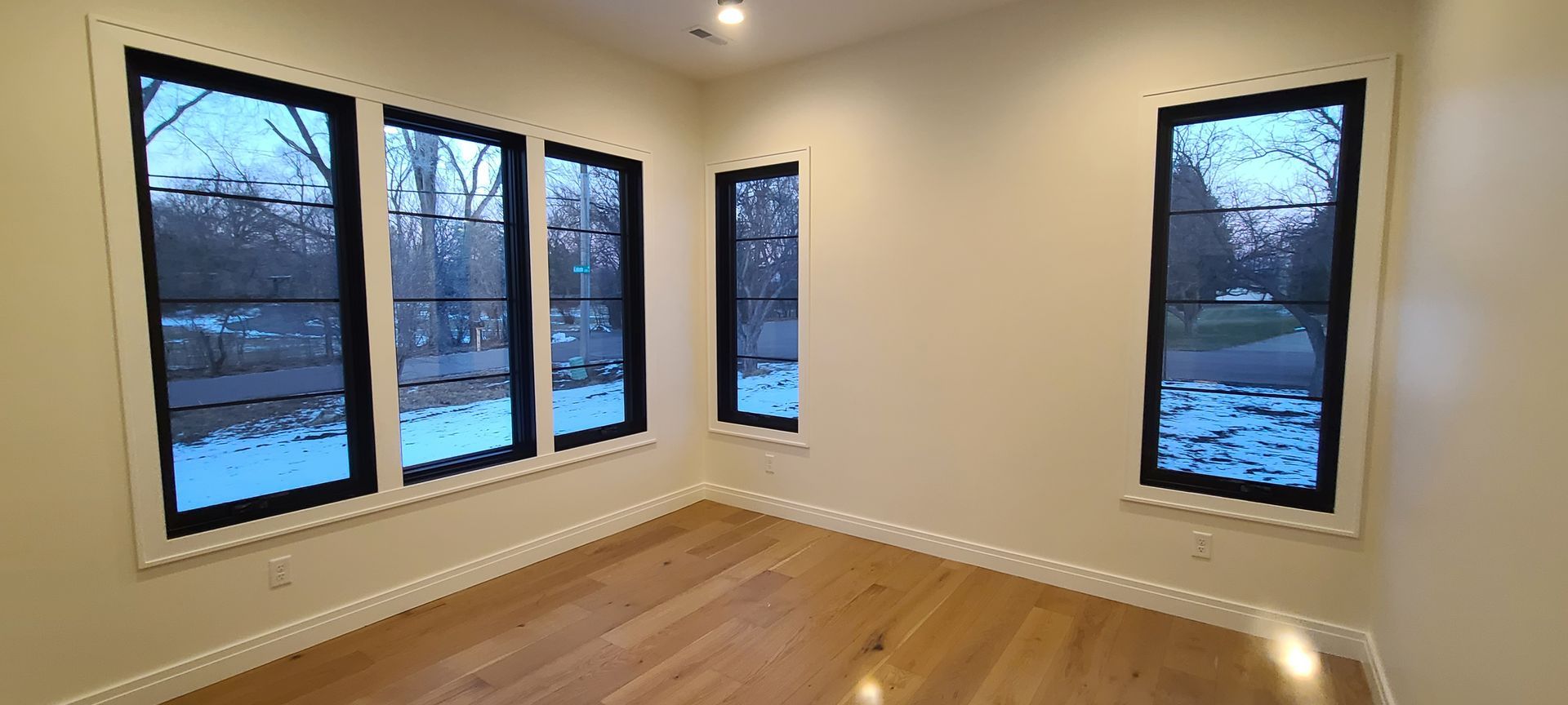 Interior view of a room with hardwood floors and multiple black-framed windows overlooking a snowy landscape.