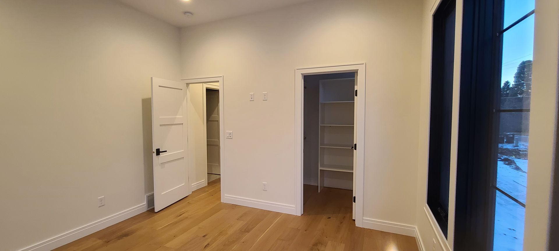 An empty room with wood floors and three doorways, including a window.