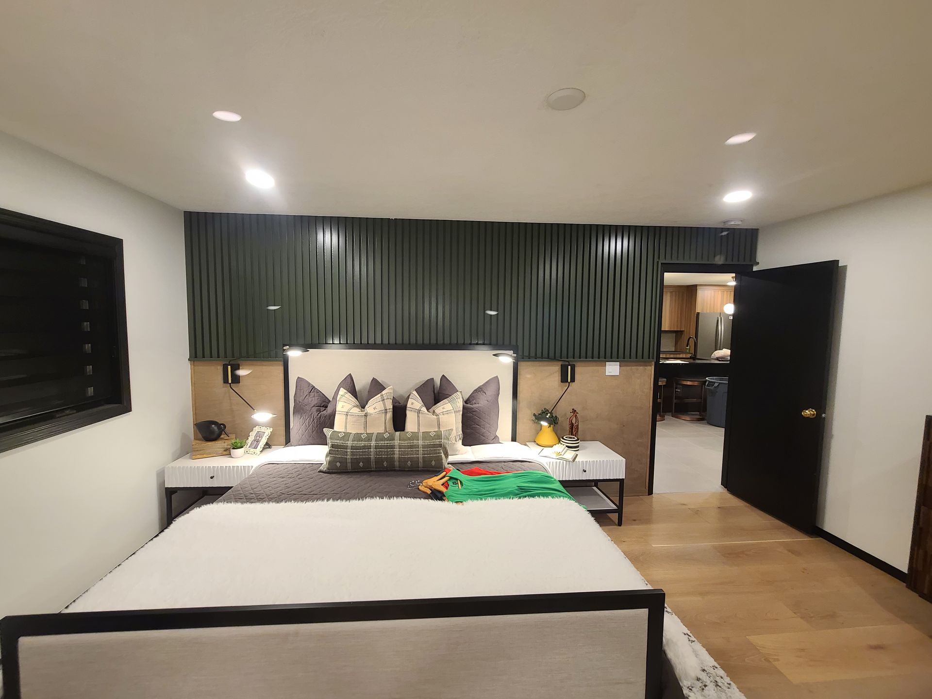 Bedroom with bed, dark green accent wall, light wood floor, and open doorway.