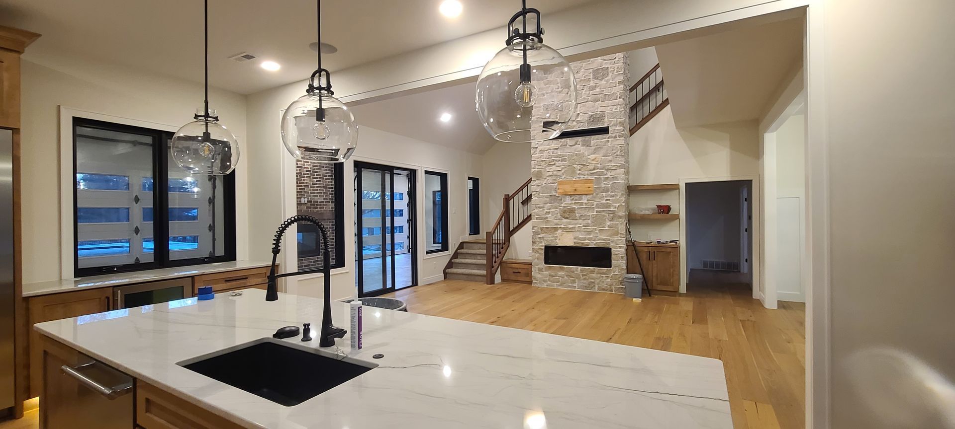 Modern open-plan kitchen and living room with white countertops, stone fireplace, and wood floors.
