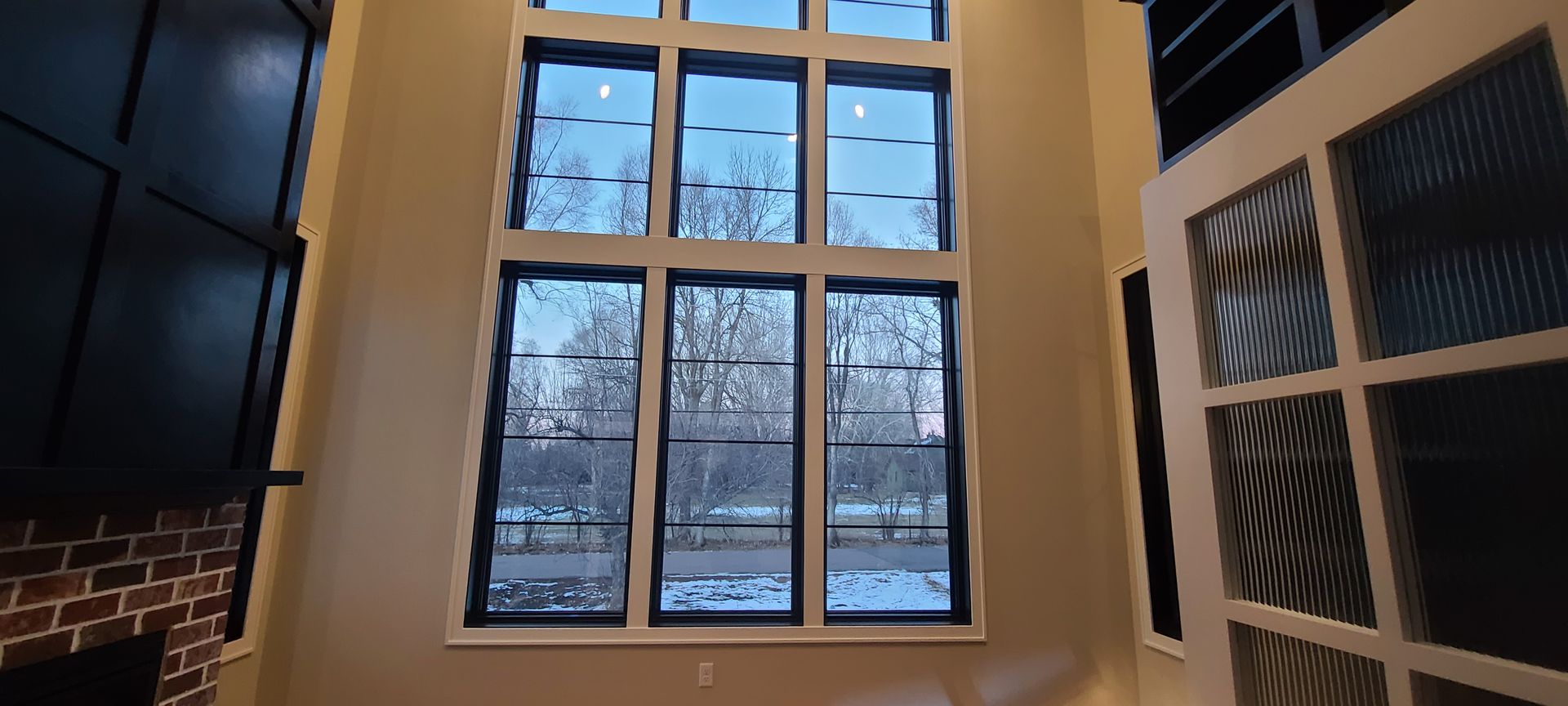 Tall windows overlooking a snowy landscape from inside a room with a fireplace.