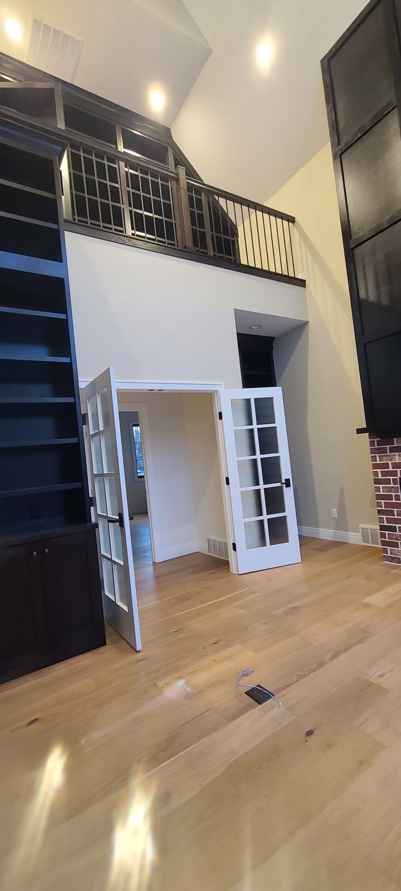 Interior with a loft, wood floor, and white French doors. A large, dark bookshelf is on the left.