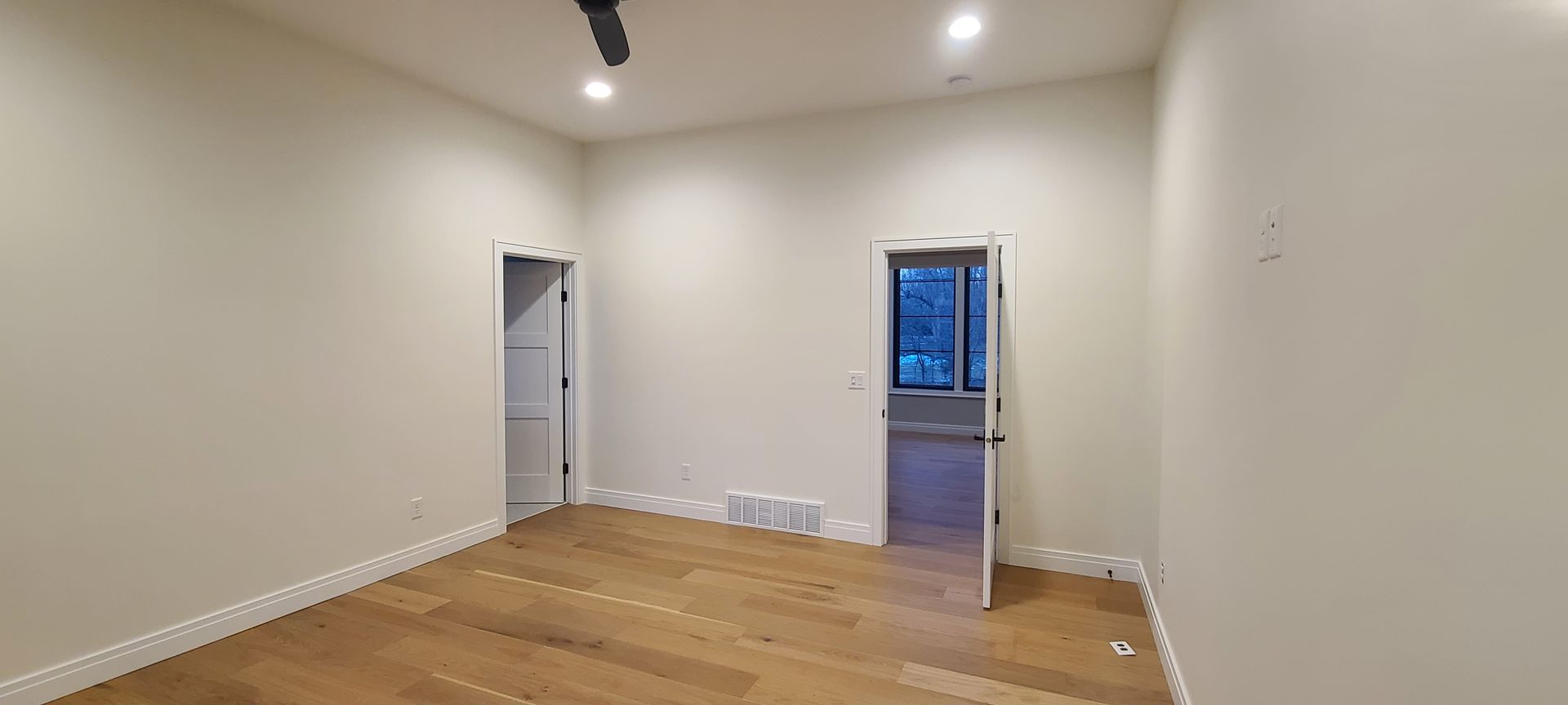 Empty room with light wood floors, two doorways, and white walls.