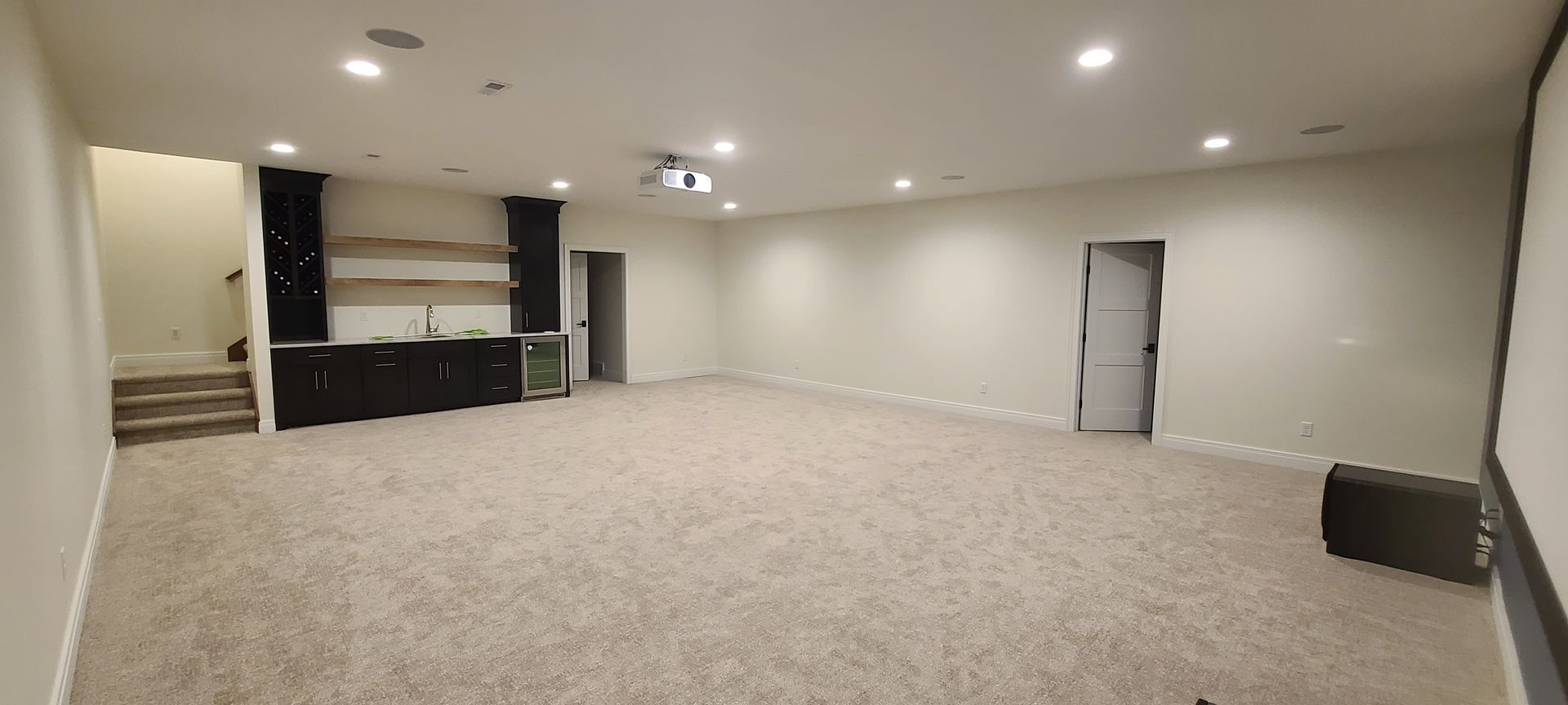Empty finished basement with a bar, steps, and recessed lighting.