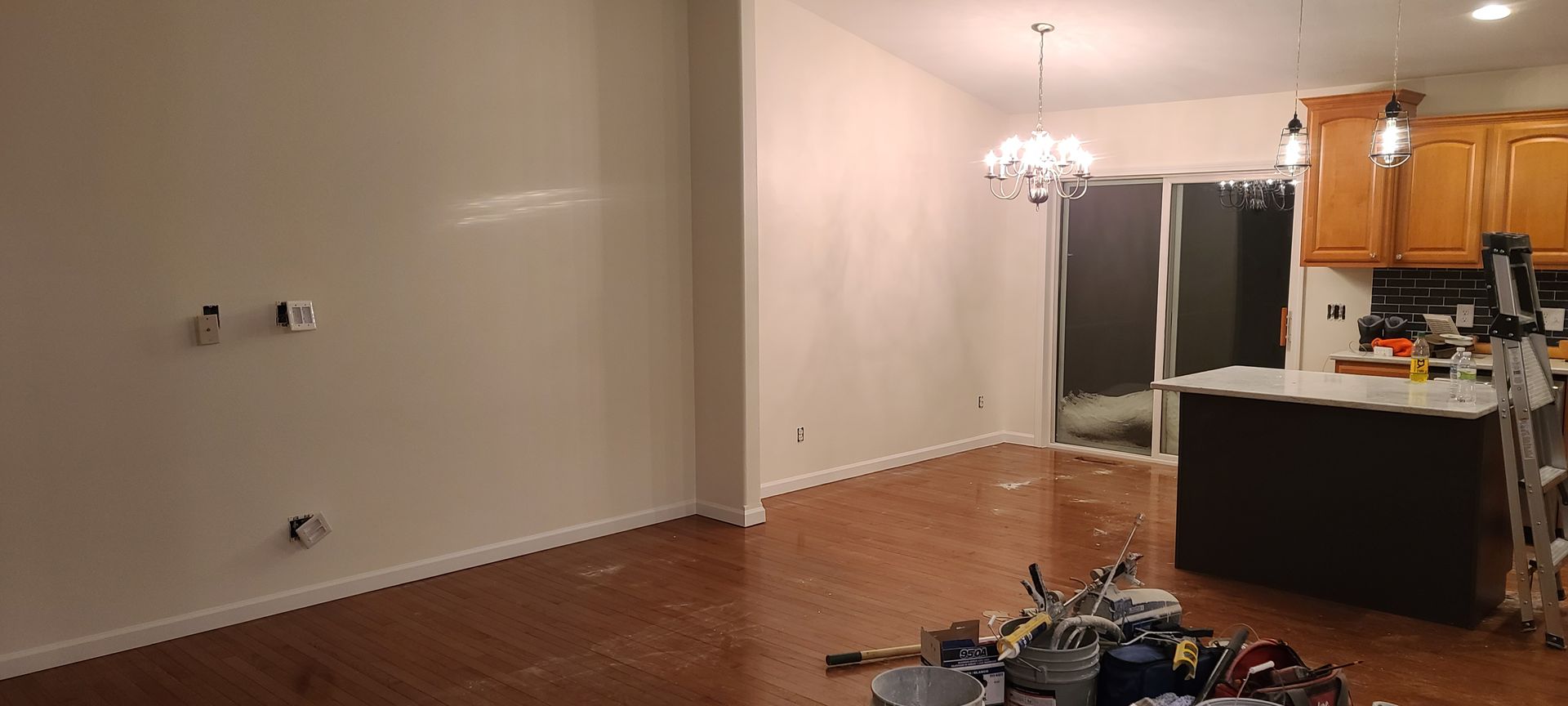 Interior view of a living room with hardwood floors, a kitchen island, and a chandelier.