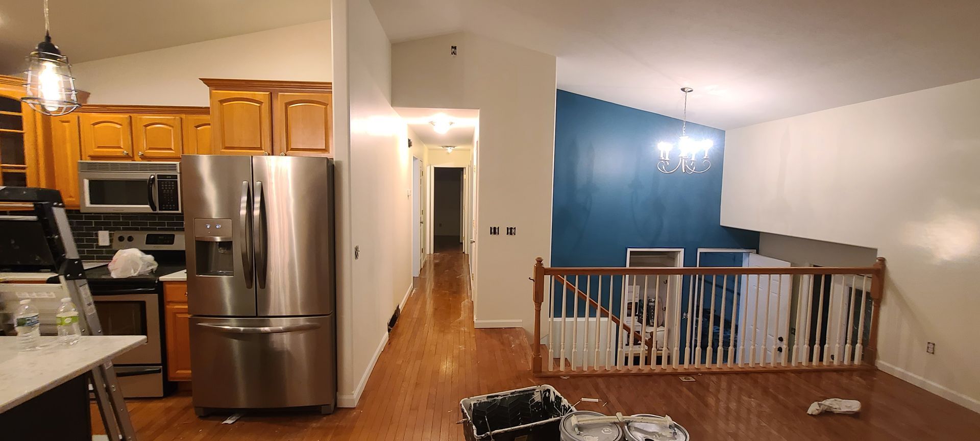 Interior view of a kitchen and living room with hardwood floors, a blue accent wall, and a stainless steel refrigerator.