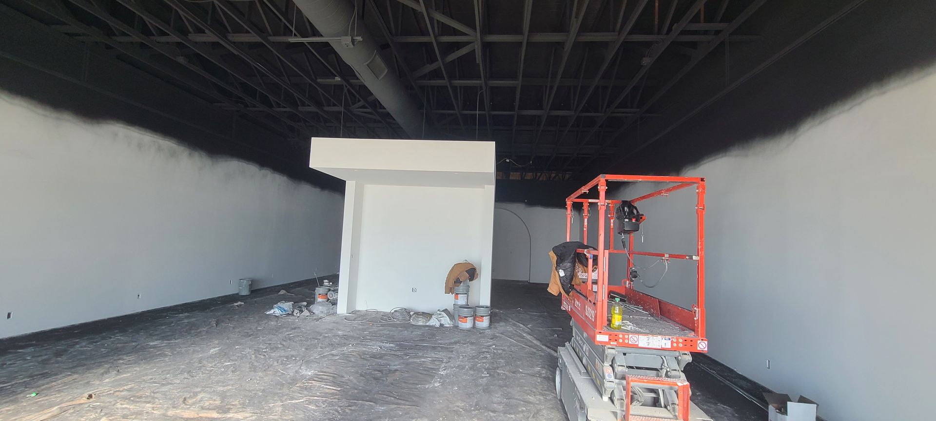 Interior view of a construction site with freshly painted white walls and black ceiling. A scissor lift is on the right.