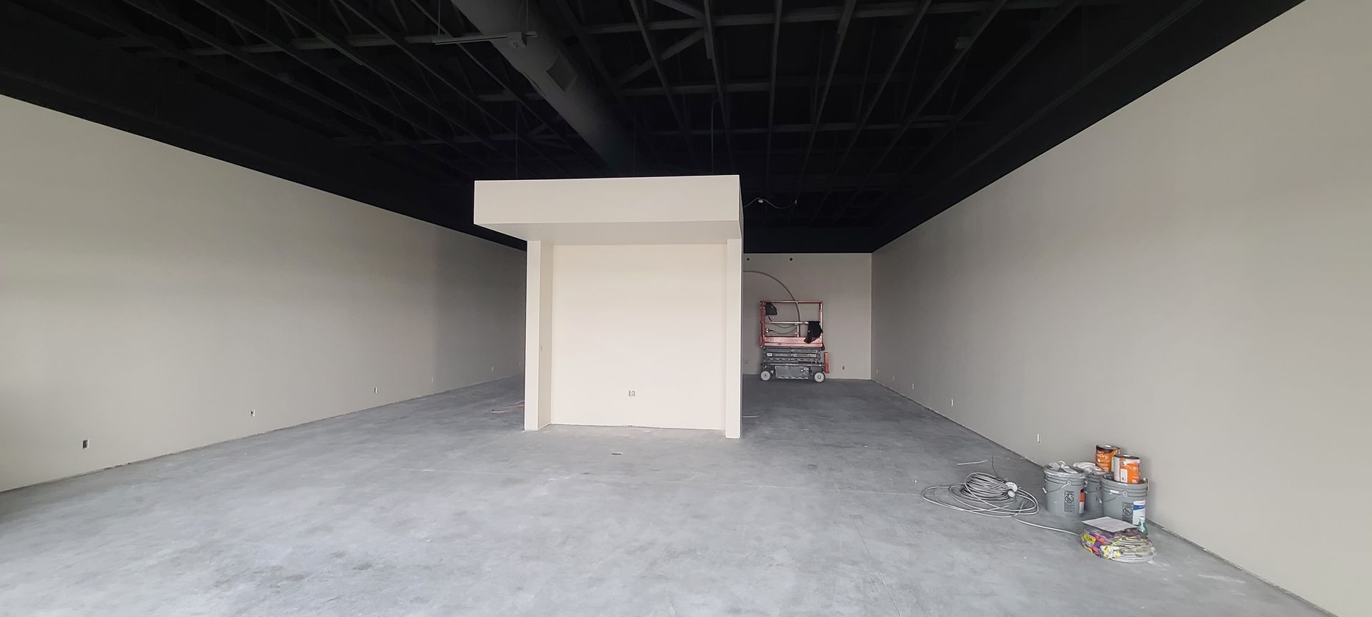Interior of an empty commercial space with concrete floor, white walls, and black ceiling.