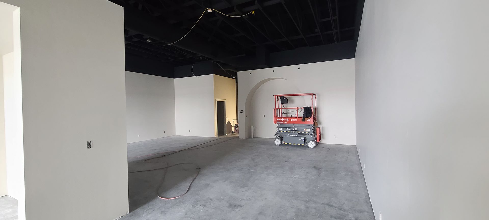 An unfinished room with a scissor lift, white walls, and a black ceiling.