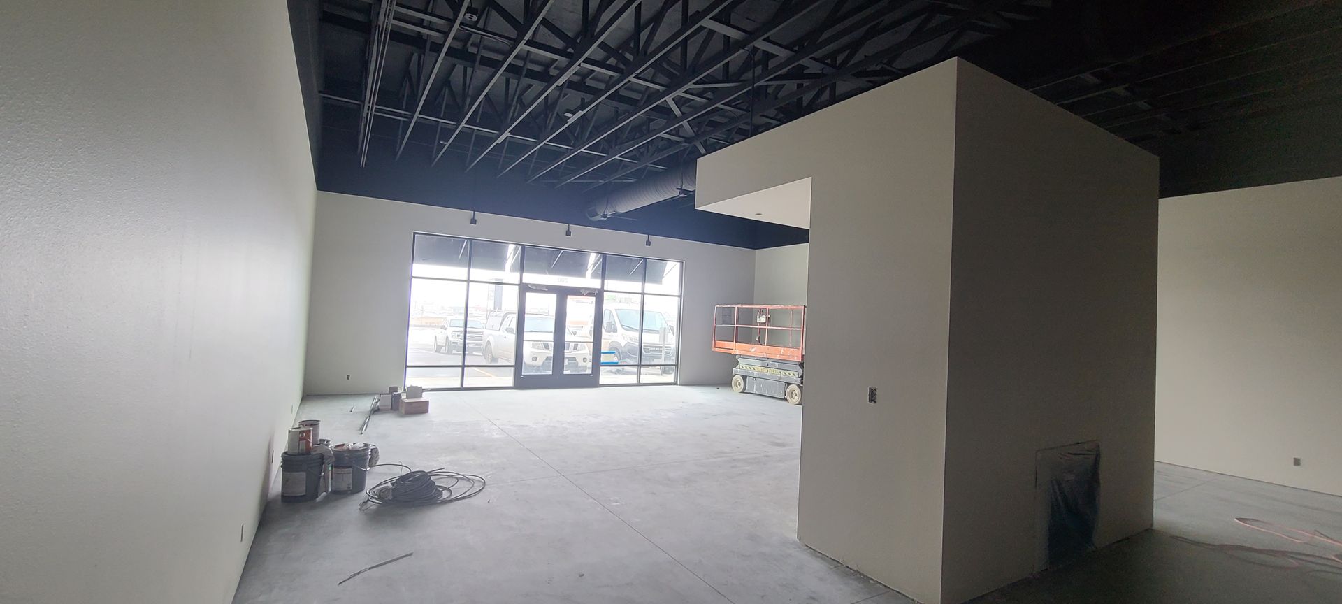 An unfinished, empty interior space with exposed ceiling beams and large windows.