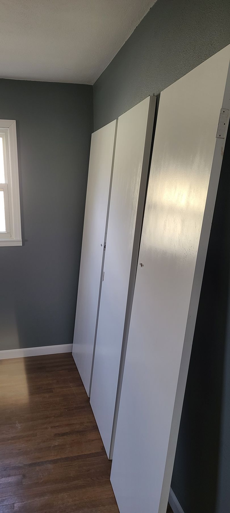 White closet doors leaning against a gray wall in a room with hardwood floors.