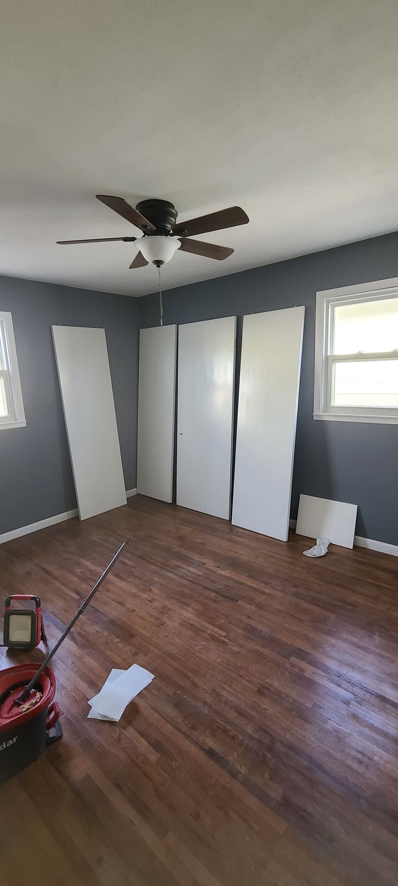 A room with wooden floors, gray walls, a ceiling fan, and white doors.