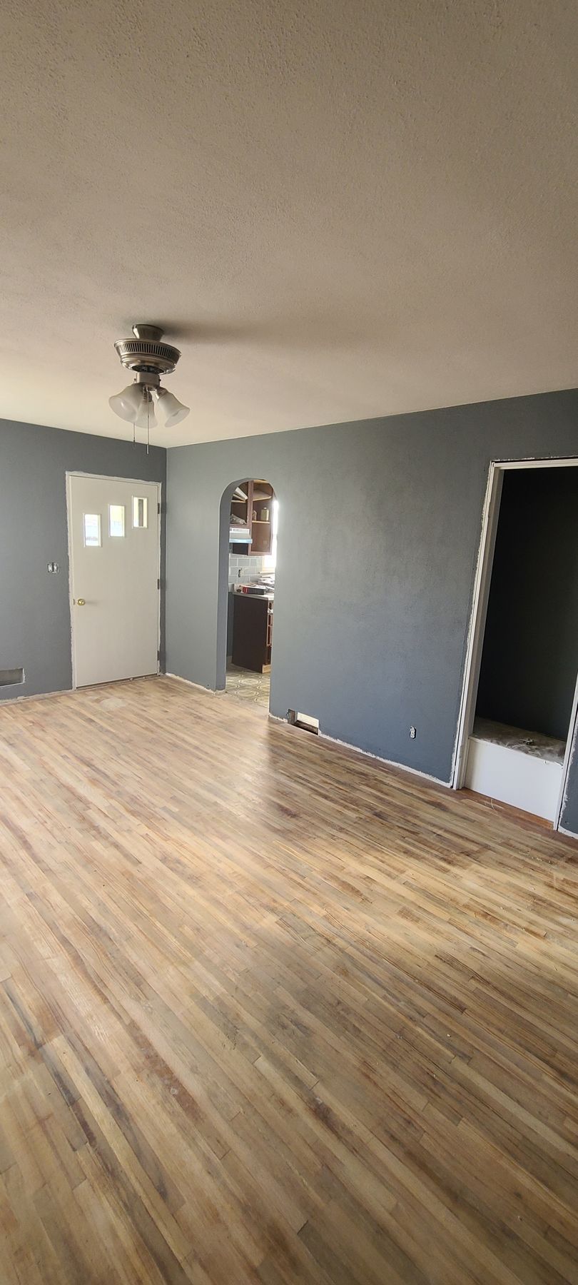 Interior of a room with hardwood floors, gray walls, and a view into a kitchen.