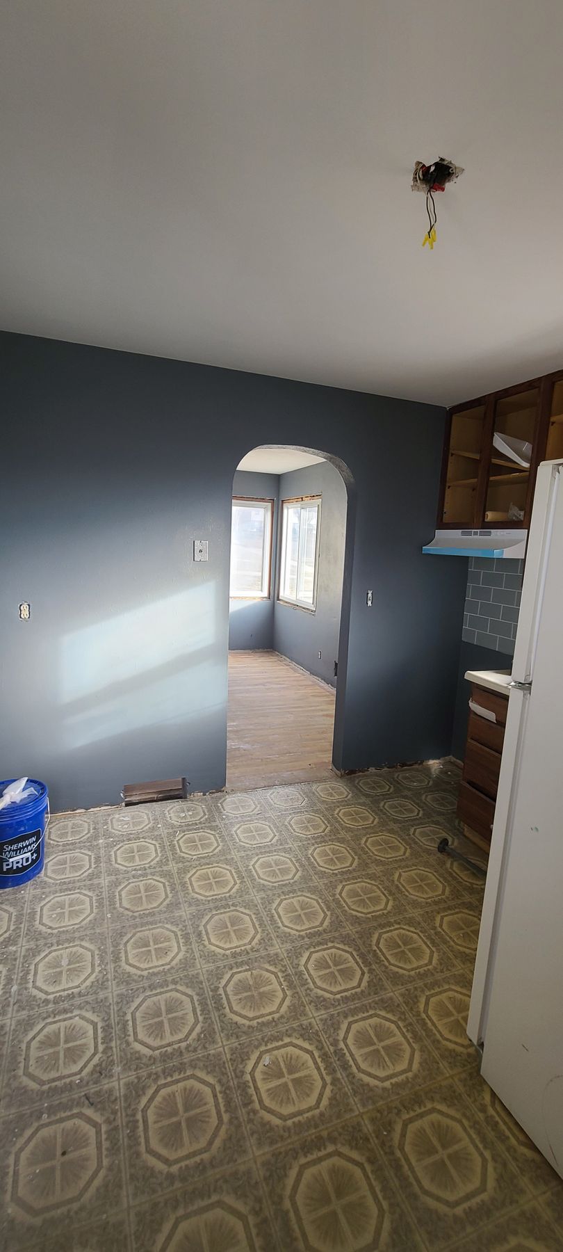 An empty kitchen with blue walls, linoleum flooring, and an archway leading to another room.