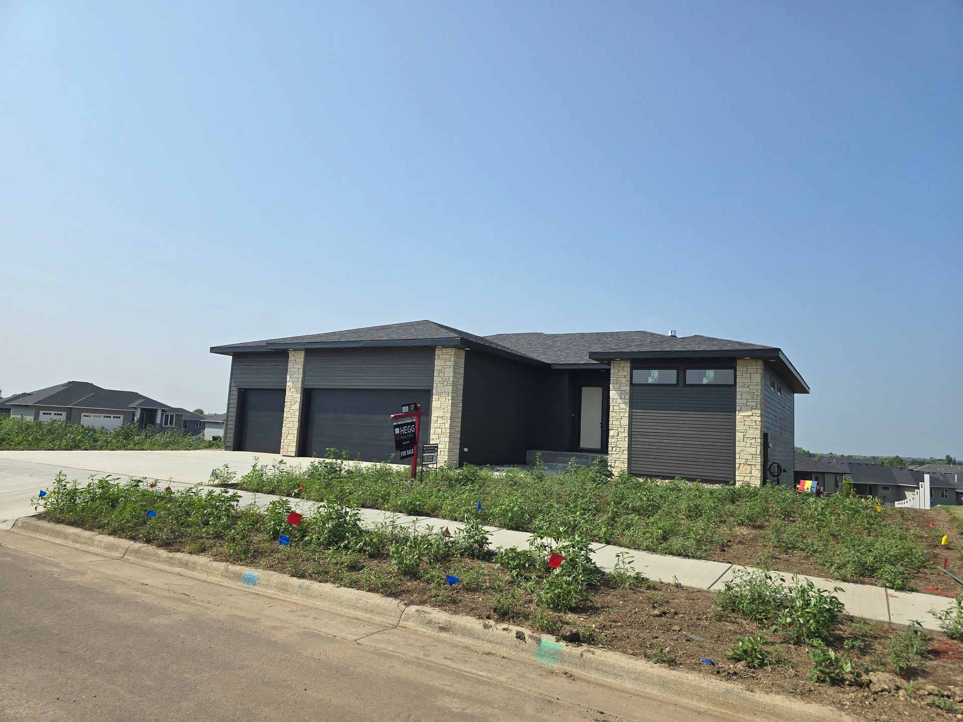 Modern house with gray siding, stone accents, two-car garage, and a concrete driveway on a sunny day.