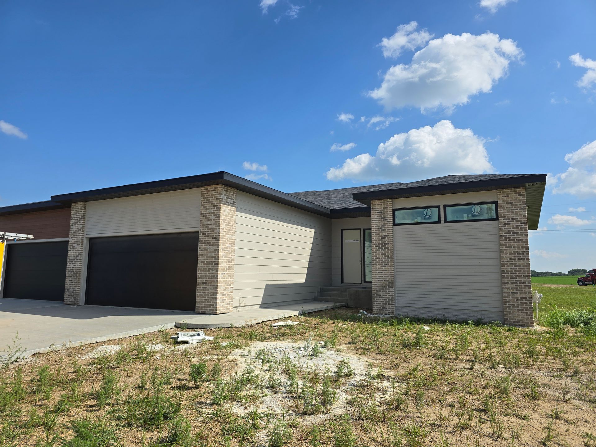 New modern home with tan siding, black garage door, and brick accents under a blue sky.
