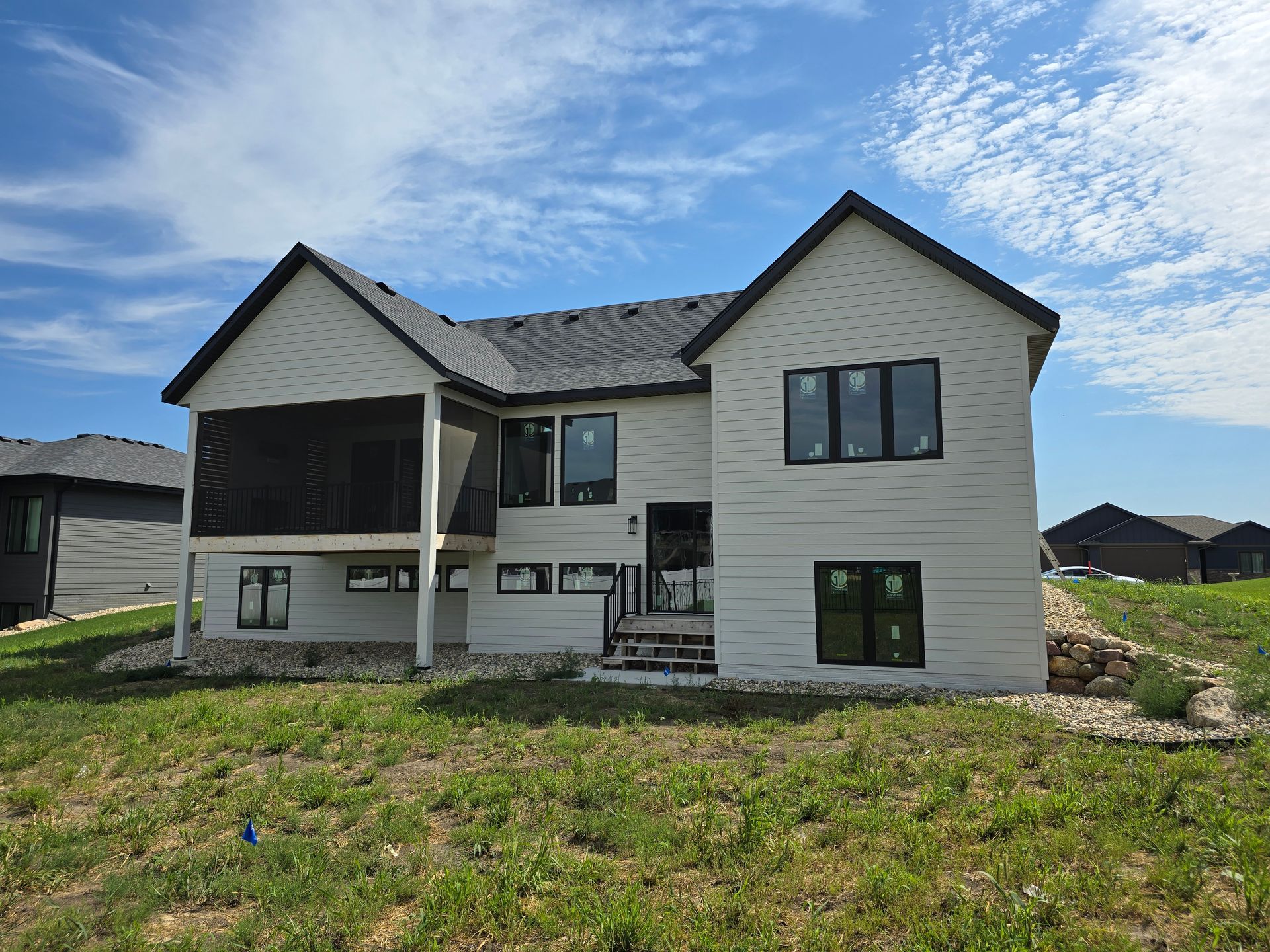 Rear view of a two-story house with light siding, black trim, and a screened porch.