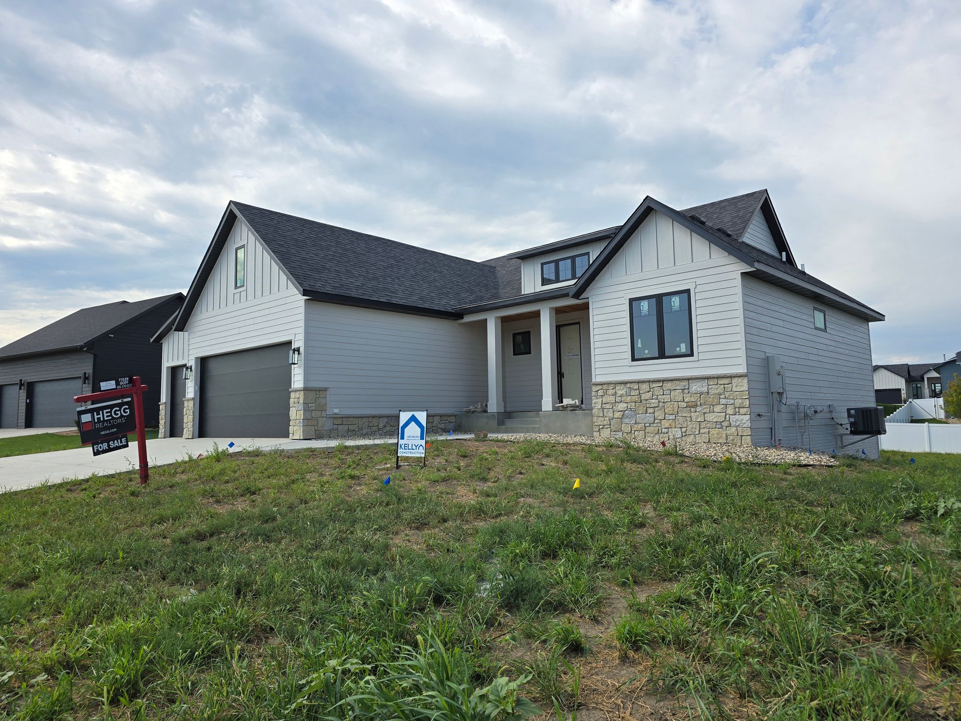 New house with gray siding, stone accents, and dark roof under a cloudy sky.