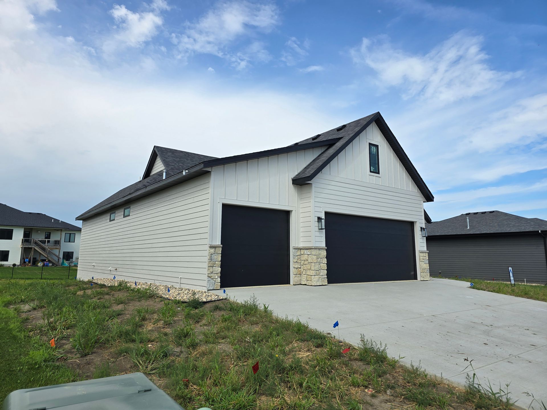 White house with black garage doors, stone accents, and dark roof under a cloudy sky.