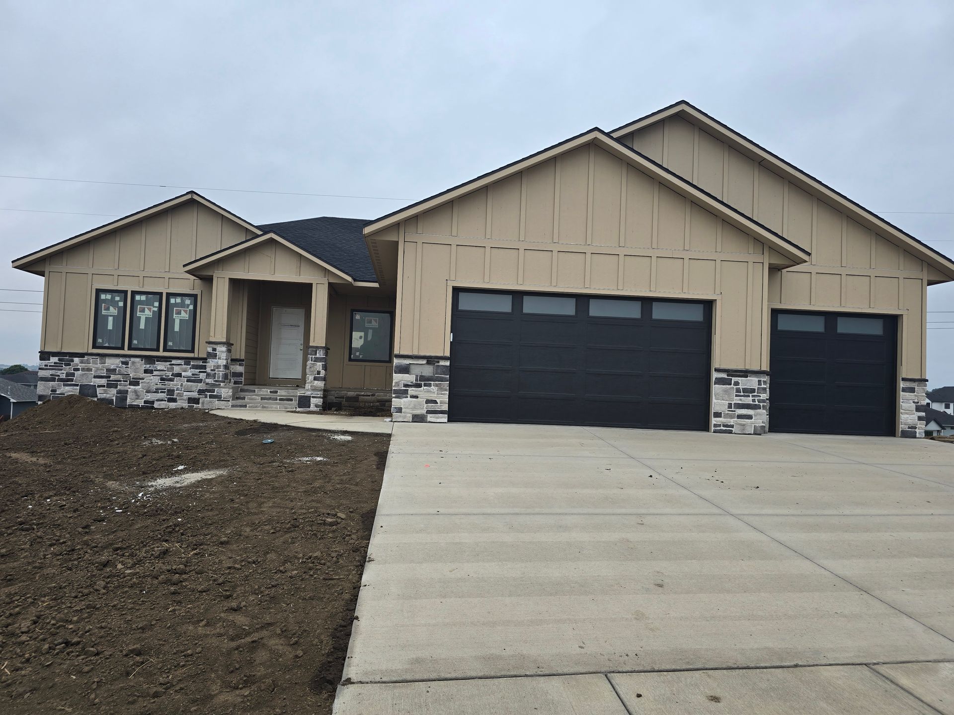 Tan and gray house with black garage doors and a concrete driveway.