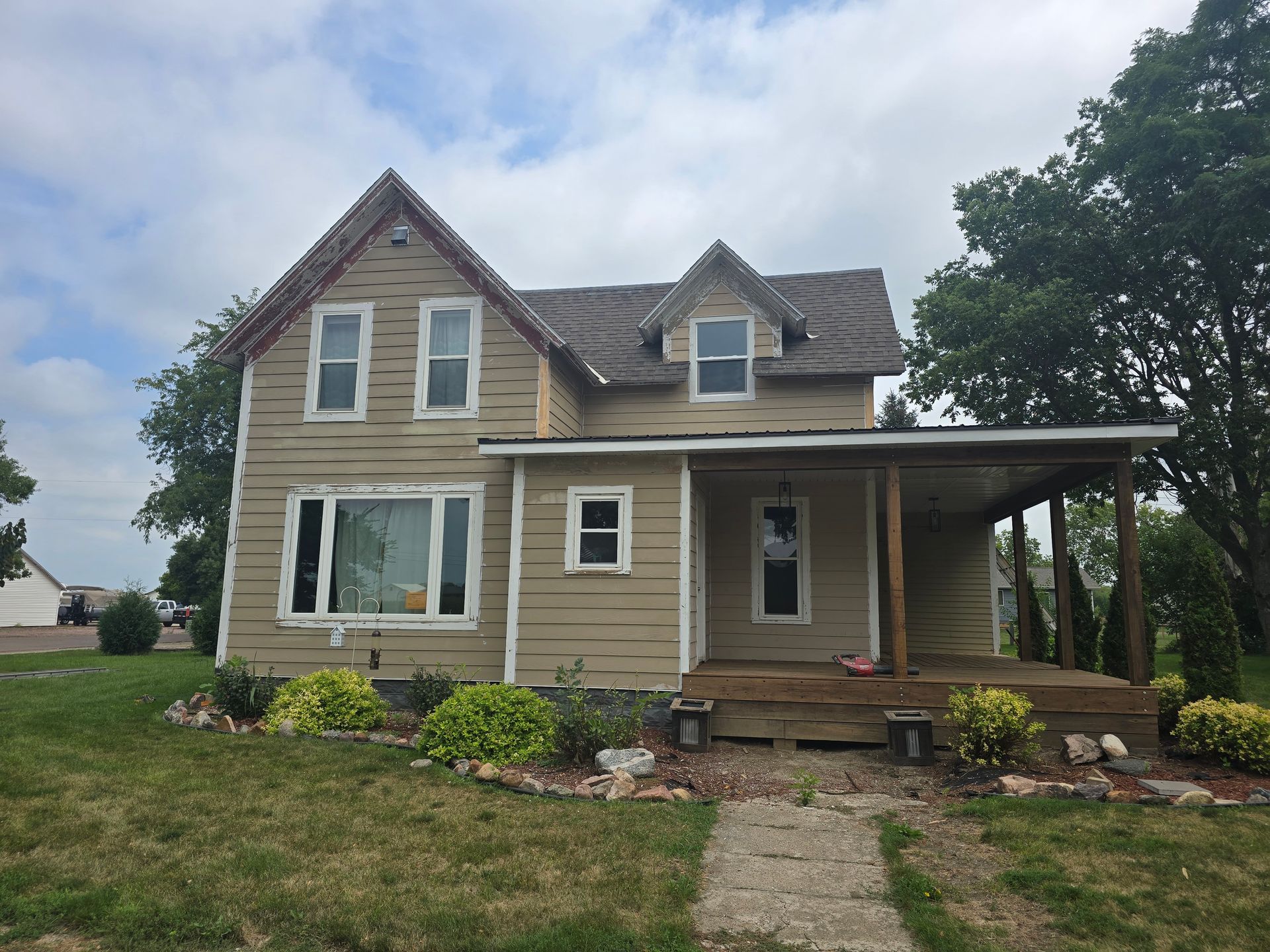 Two-story, beige house with porch, visible windows, and a cloudy sky background.
