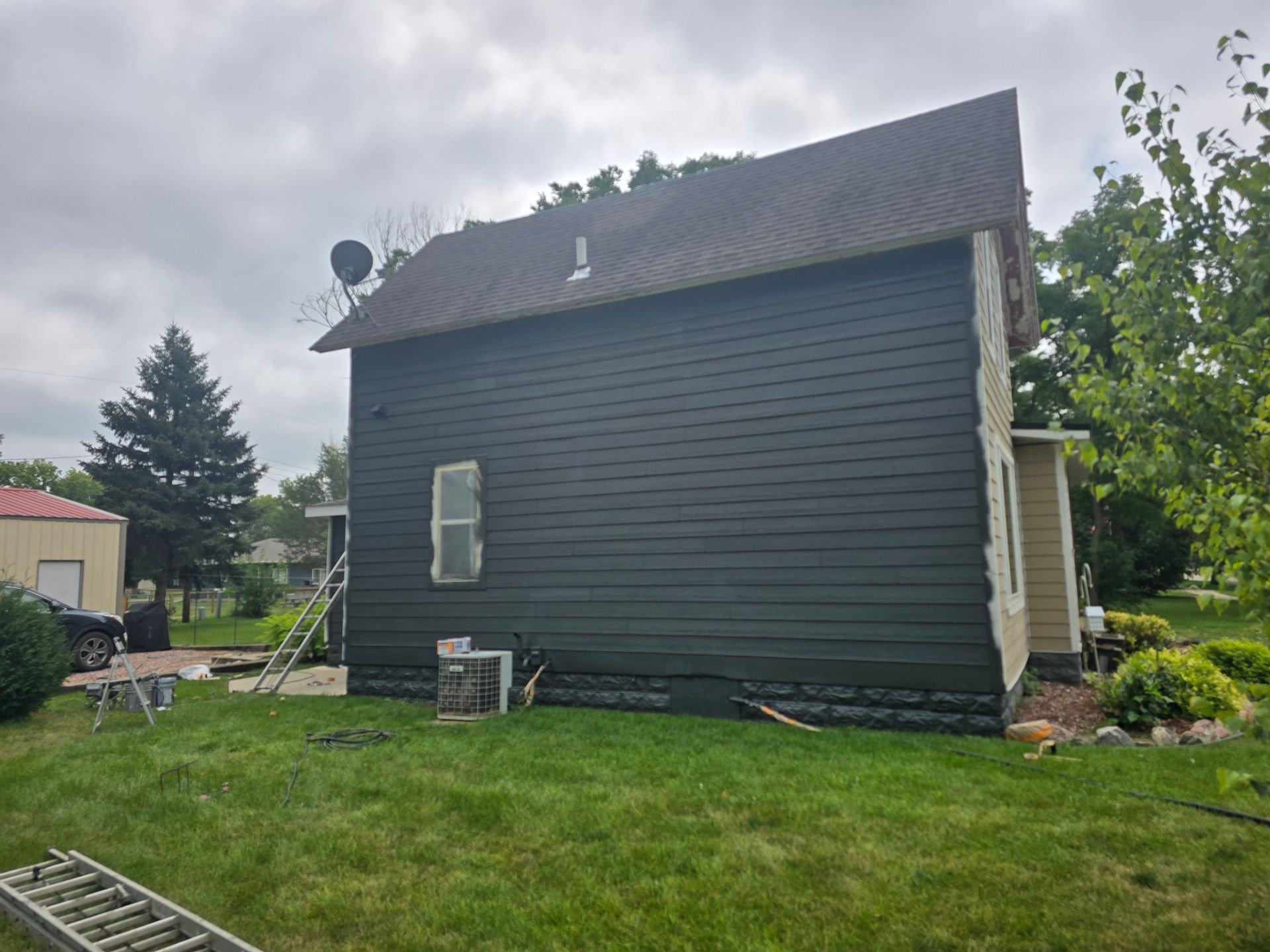 Black house exterior; green lawn. Overcast sky.