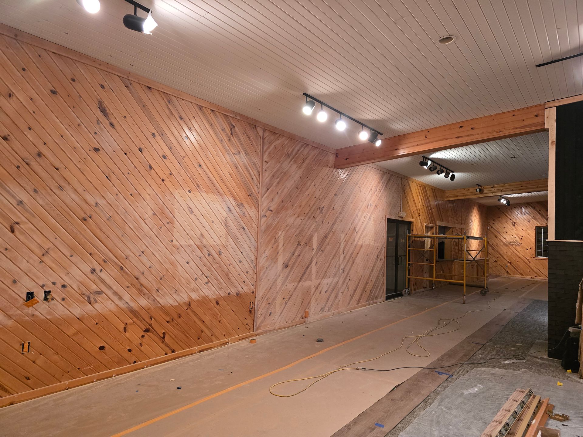 Empty room with angled wooden panel walls, track lighting, and a doorway to another room.