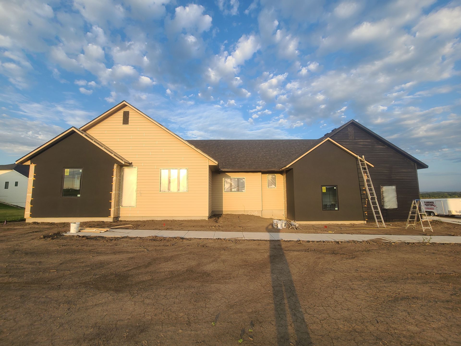 A partially constructed house with tan siding and black accents under a blue sky.