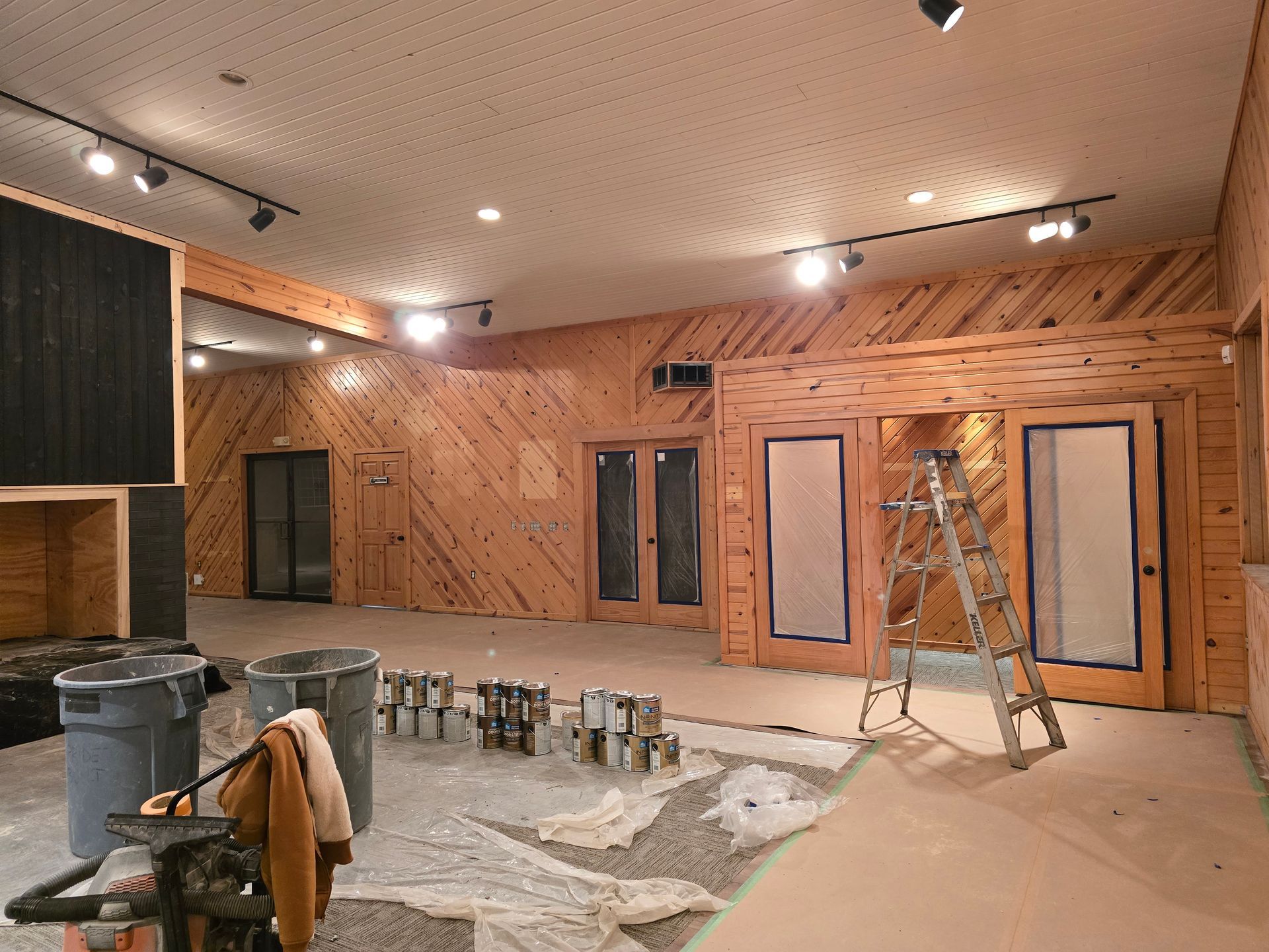 Interior room renovation with wood paneling, paint cans, and a ladder.