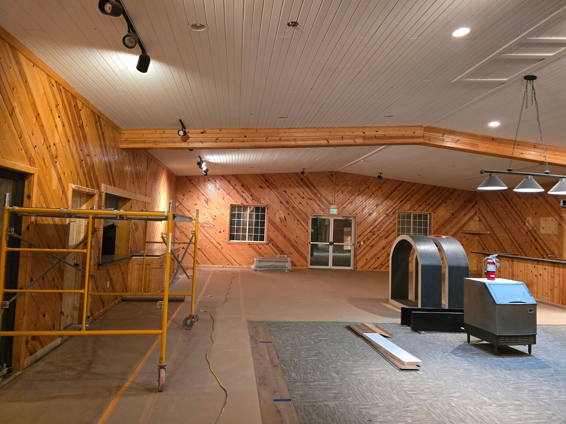 Interior of a room with wood paneling and exposed beams. Scaffolding, windows, and equipment visible.