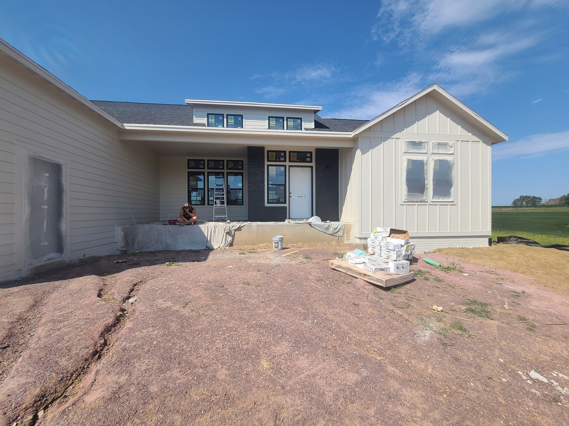 House under construction, exterior view. Beige siding, dark roof, porch, and unfinished landscaping.