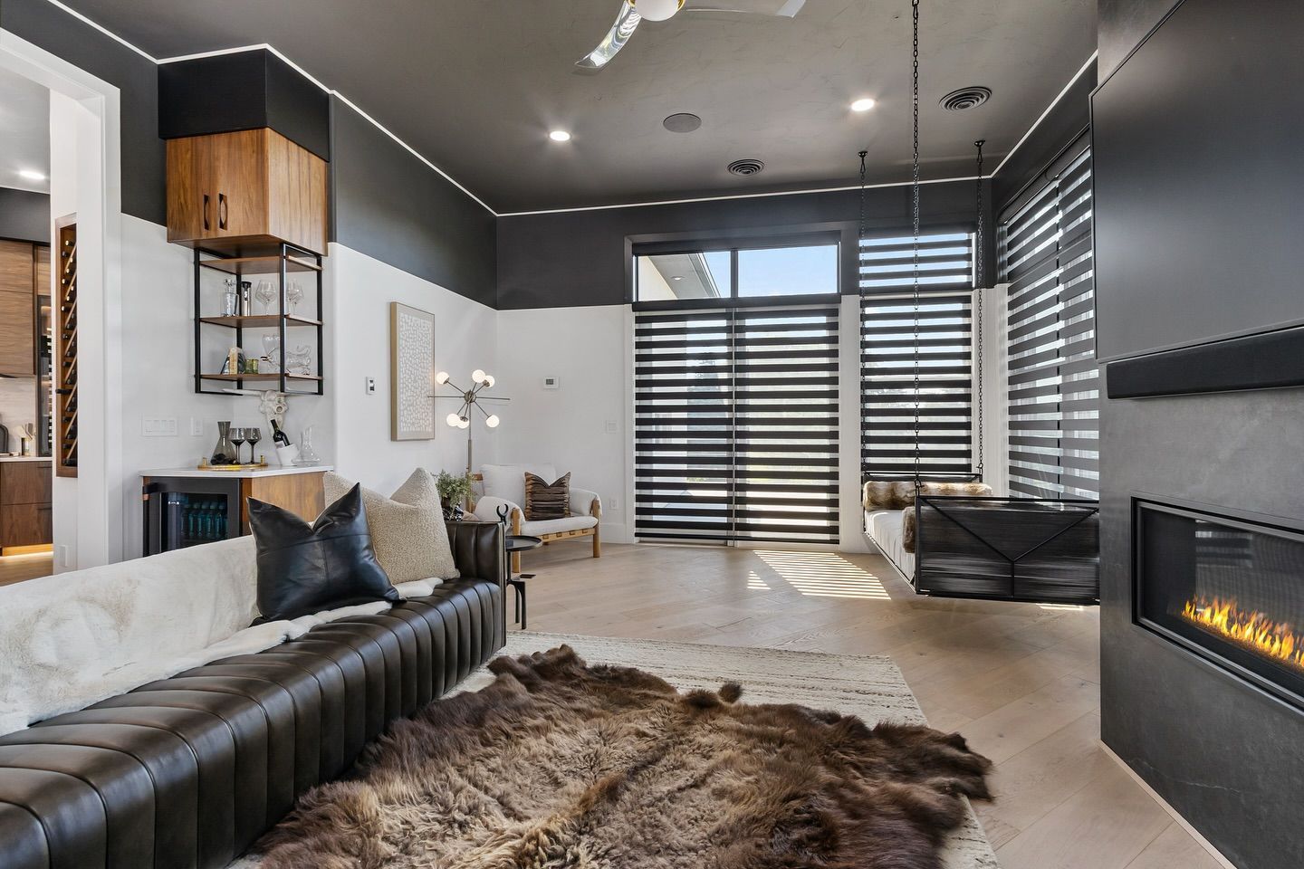 Modern living room with leather couch, fireplace, large windows, and fur rug.
