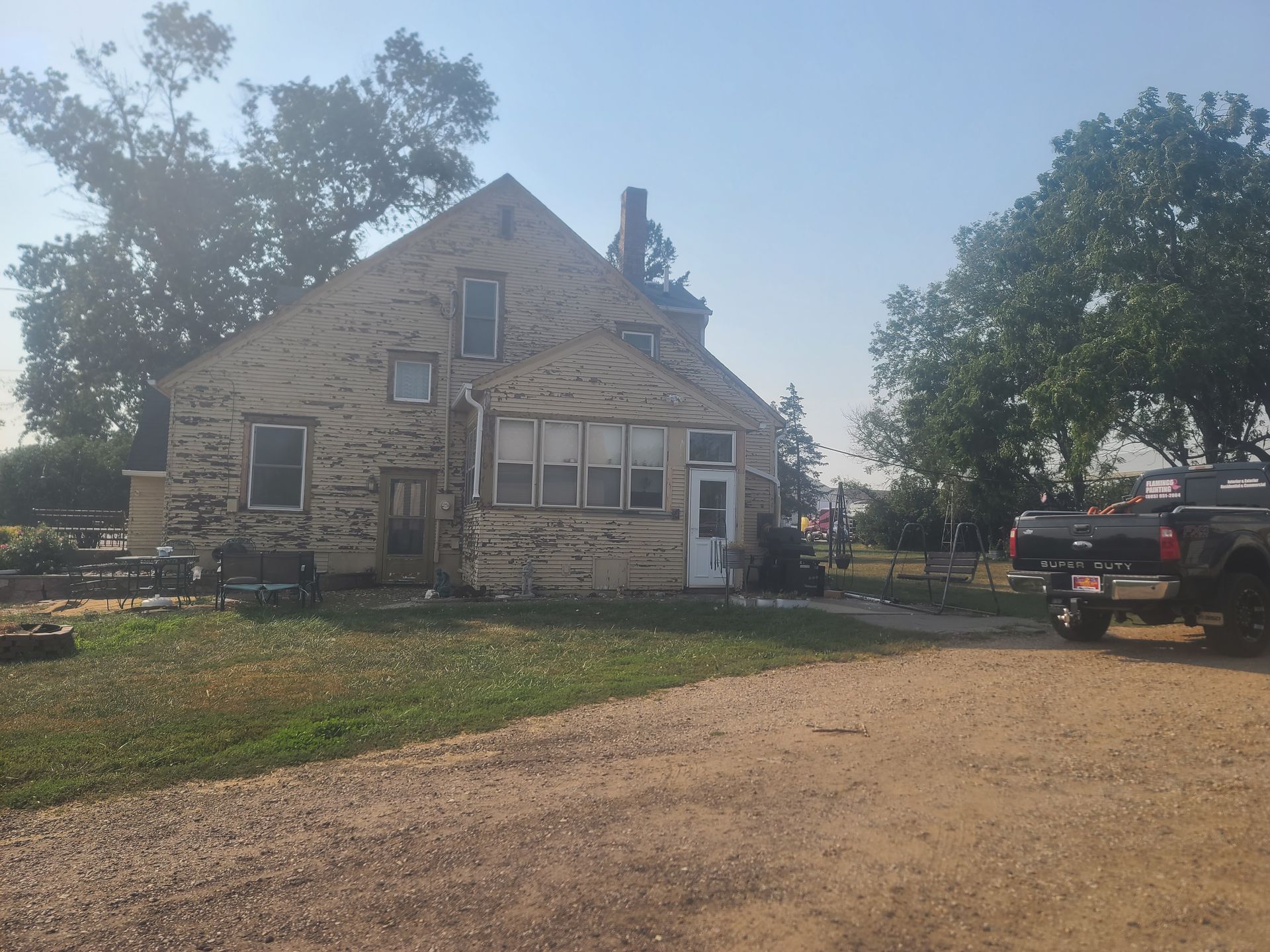 Dilapidated wooden house with peeling paint, front door, windows, and dirt driveway.