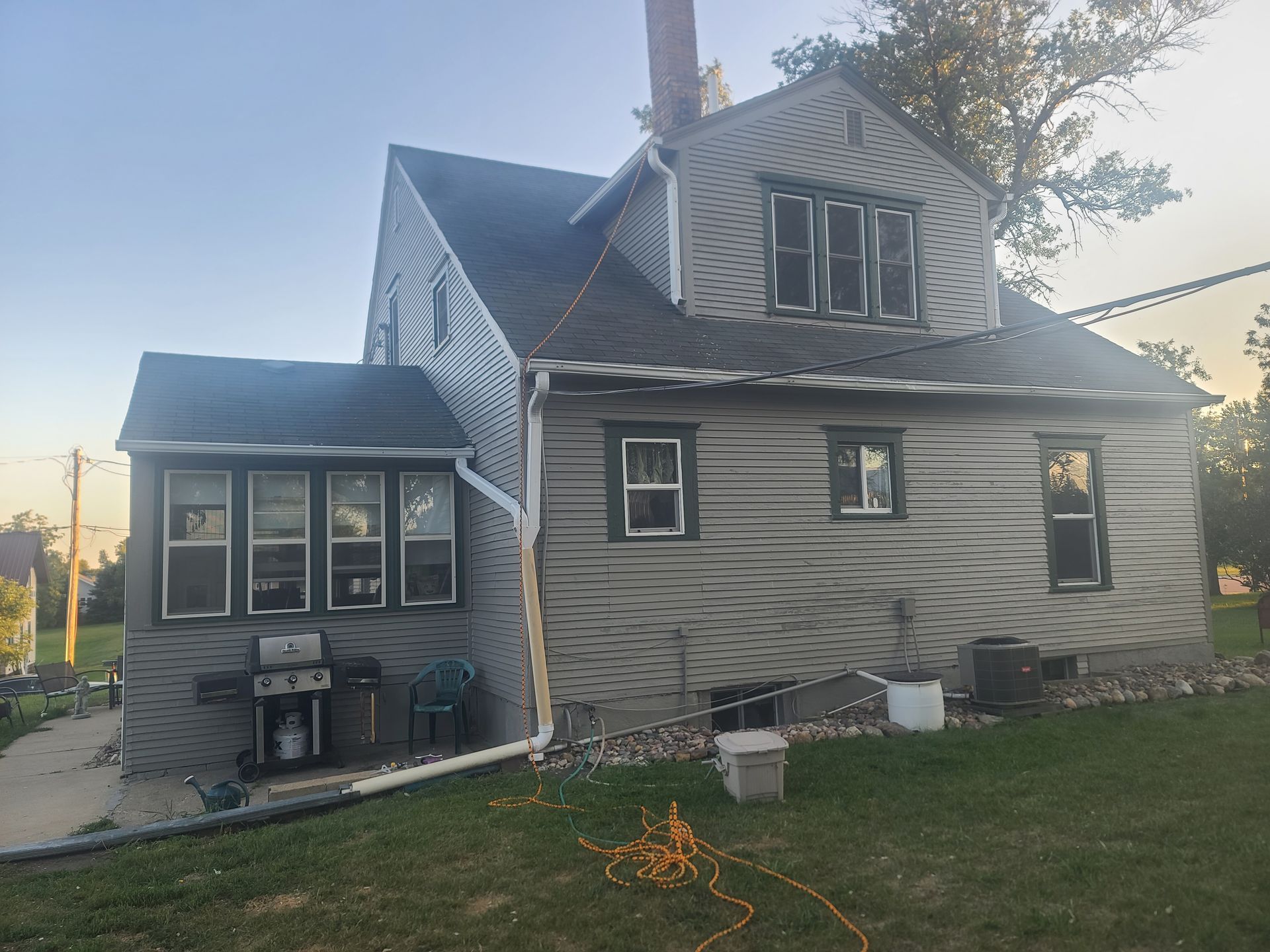 Gray house with bay window, siding, dark windows, chimney, and green yard.