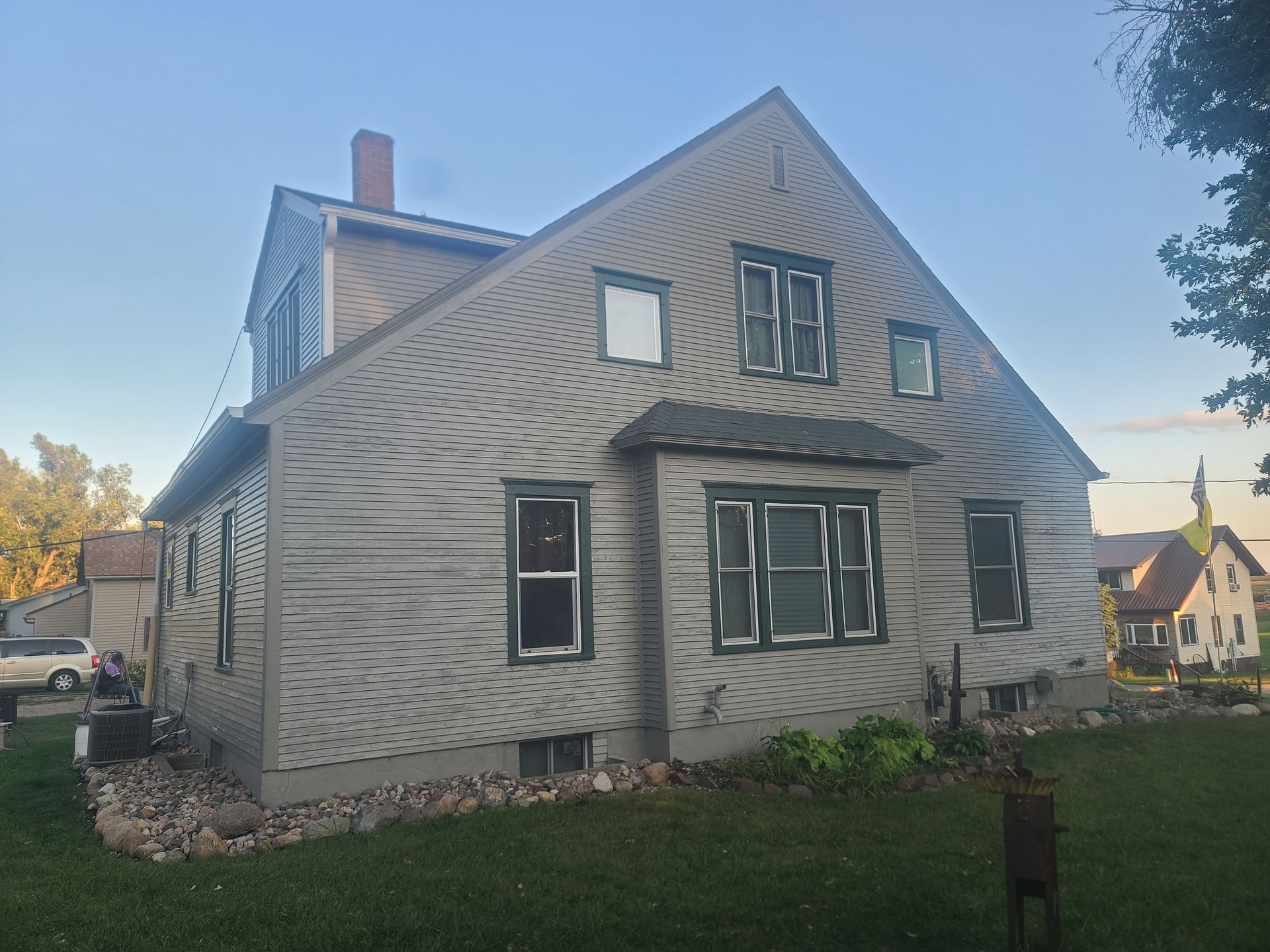 Two-story house with light siding and green window frames, set on a grassy lawn.
