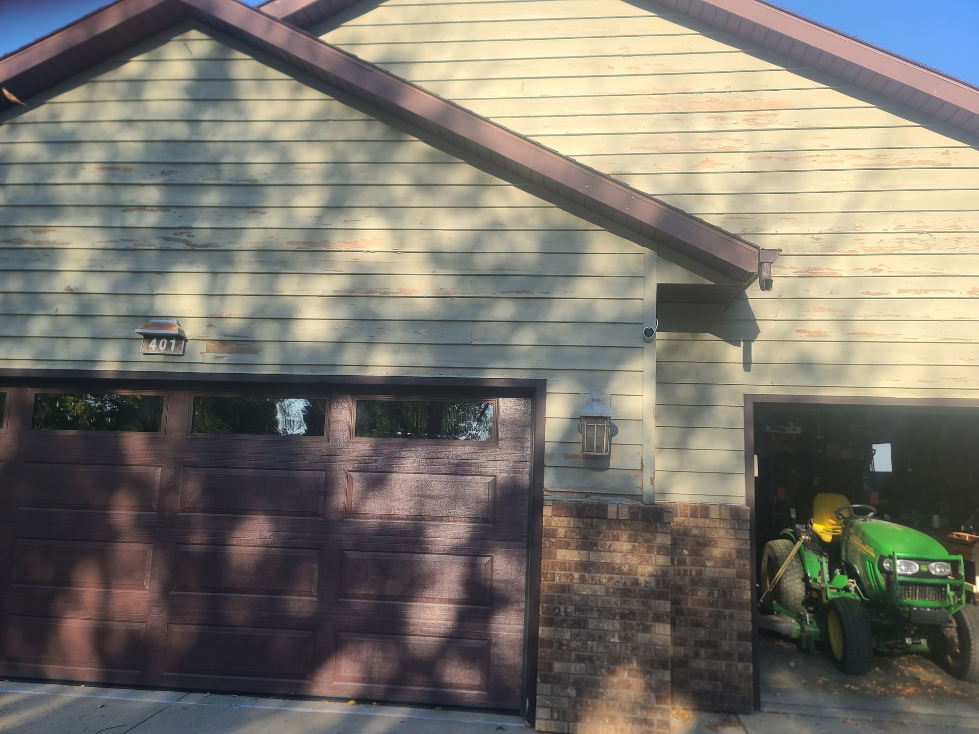 Tan house with brown garage door, open right garage showing a green tractor.