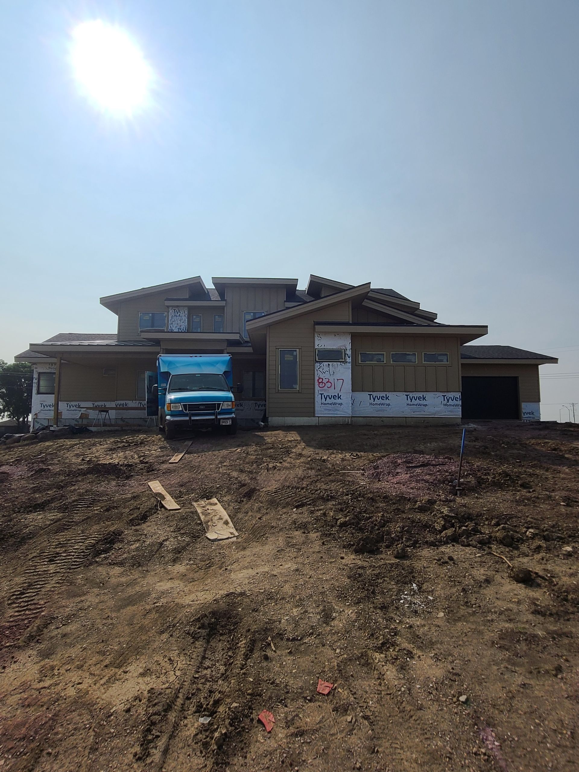 Construction site: partially built modern house with blue truck in front, under a bright sun.