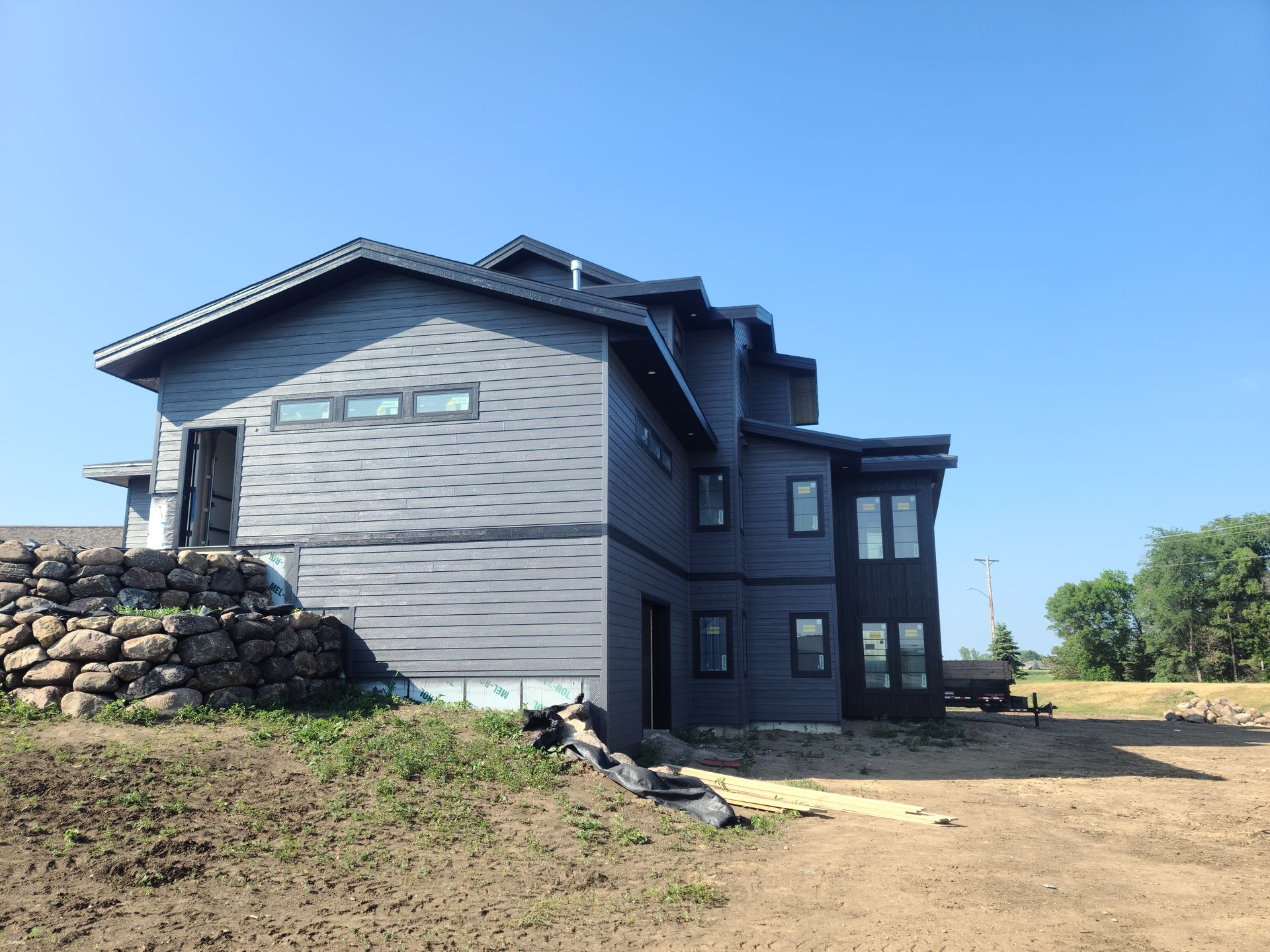 Dark gray house under construction, blue sky, and a rock wall.