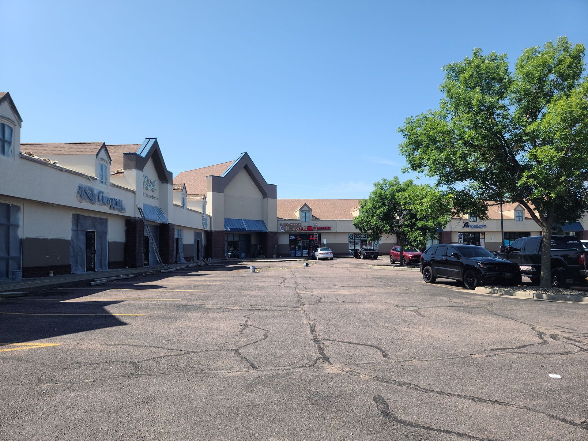 A strip mall with businesses, parking lot, and parked cars under a clear, blue sky.