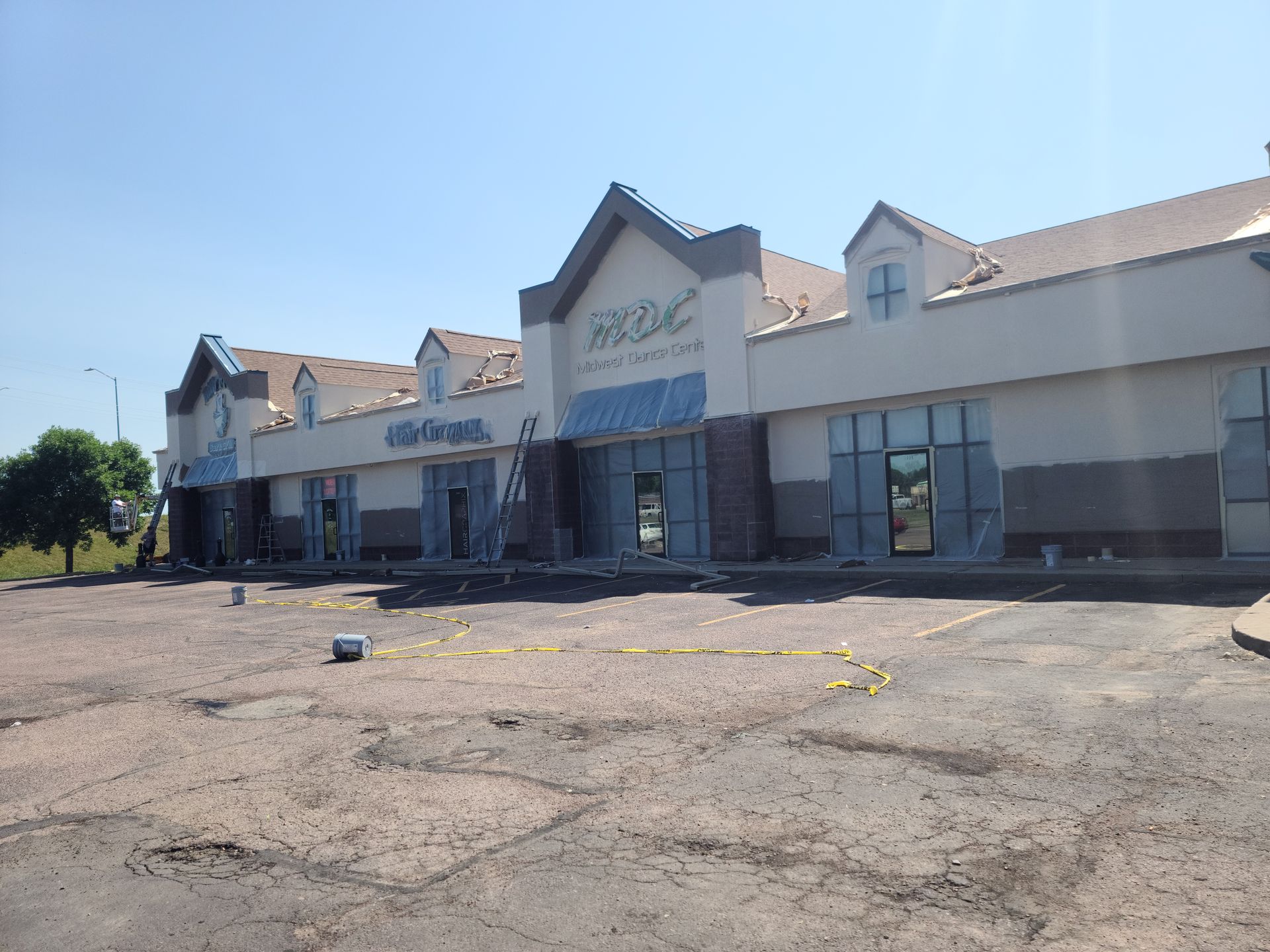 Exterior view of a shopping center with ongoing construction. Buildings are white with blue accents and a faded parking lot.