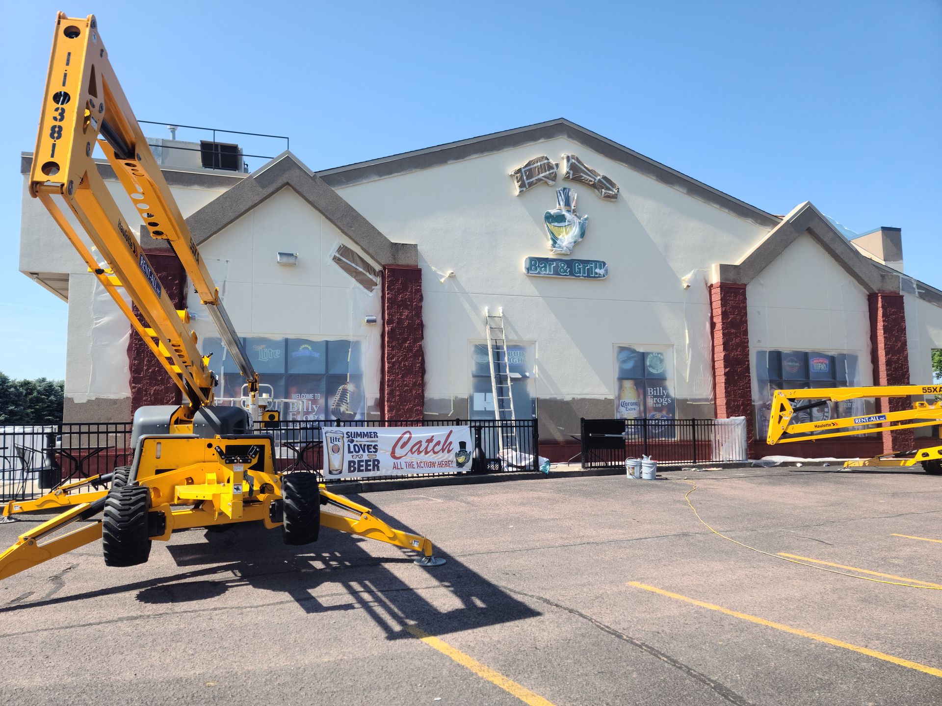 Exterior of restaurant being painted; yellow lift machinery in parking lot.