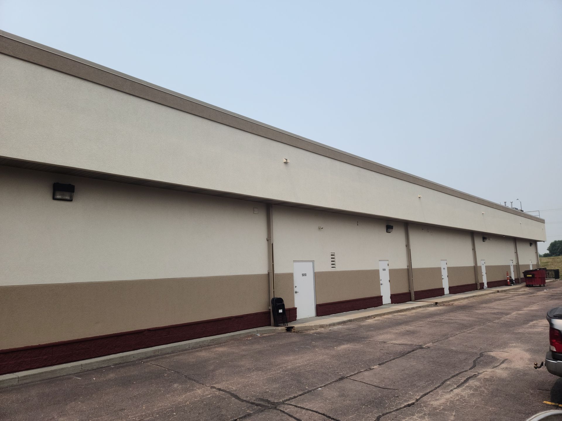 Long tan and brown building with several white doors along the wall.