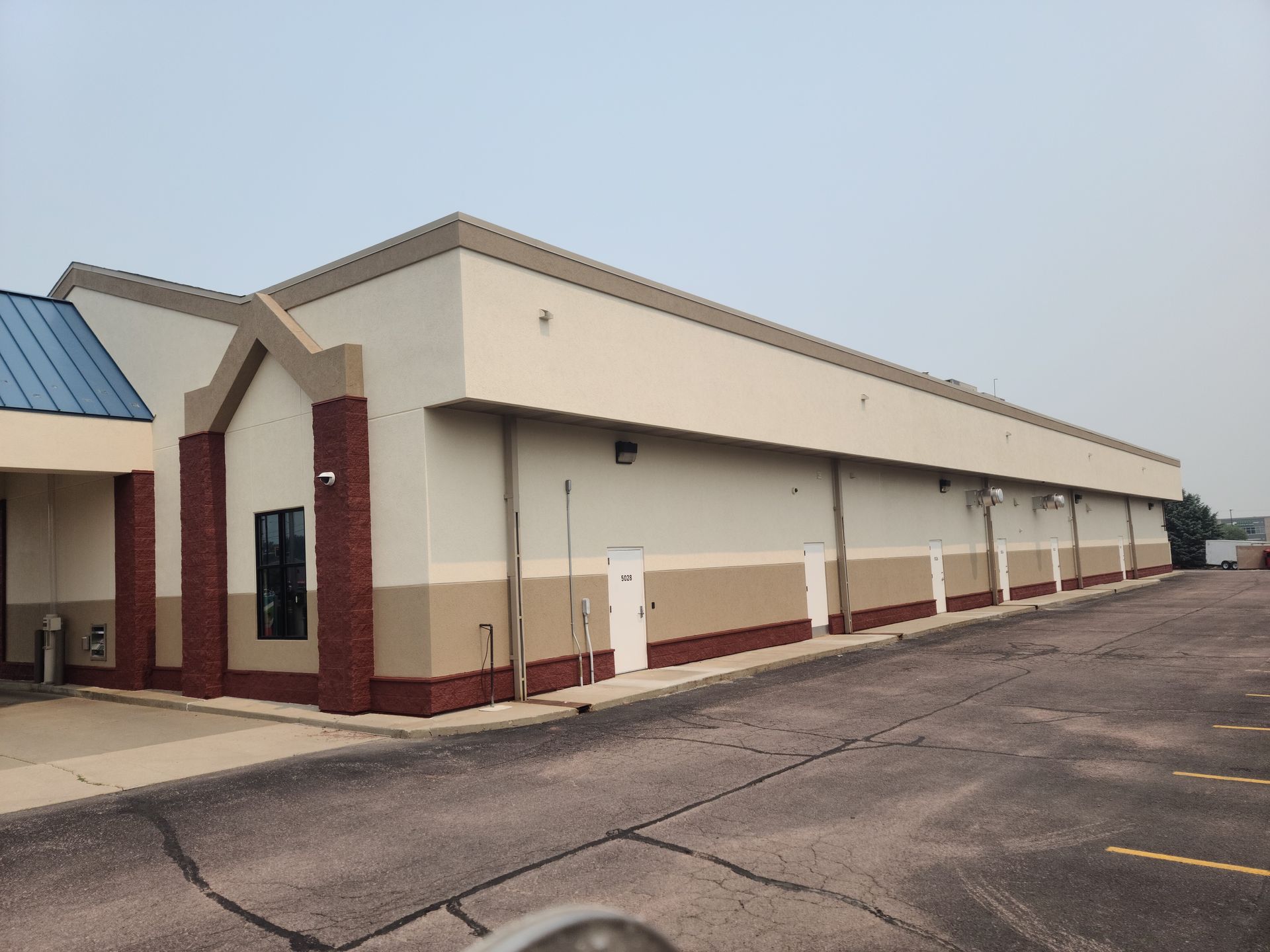 A long beige and tan commercial building with dark pavement in front.