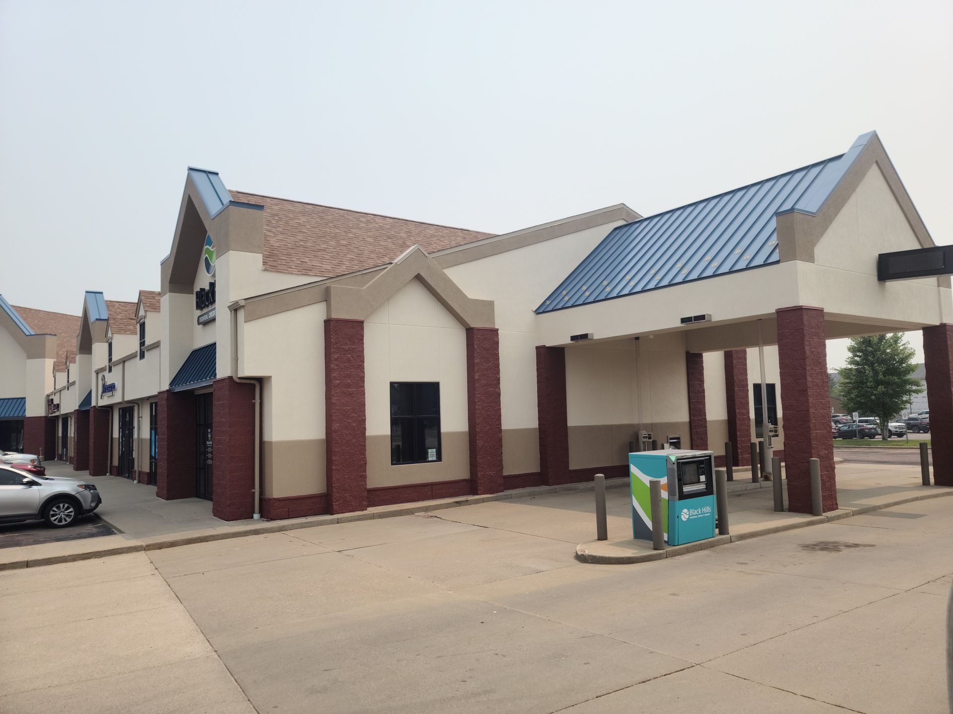 Bank building with drive-thru, tan and red brick exterior, blue metal roof. A parked car is in front.