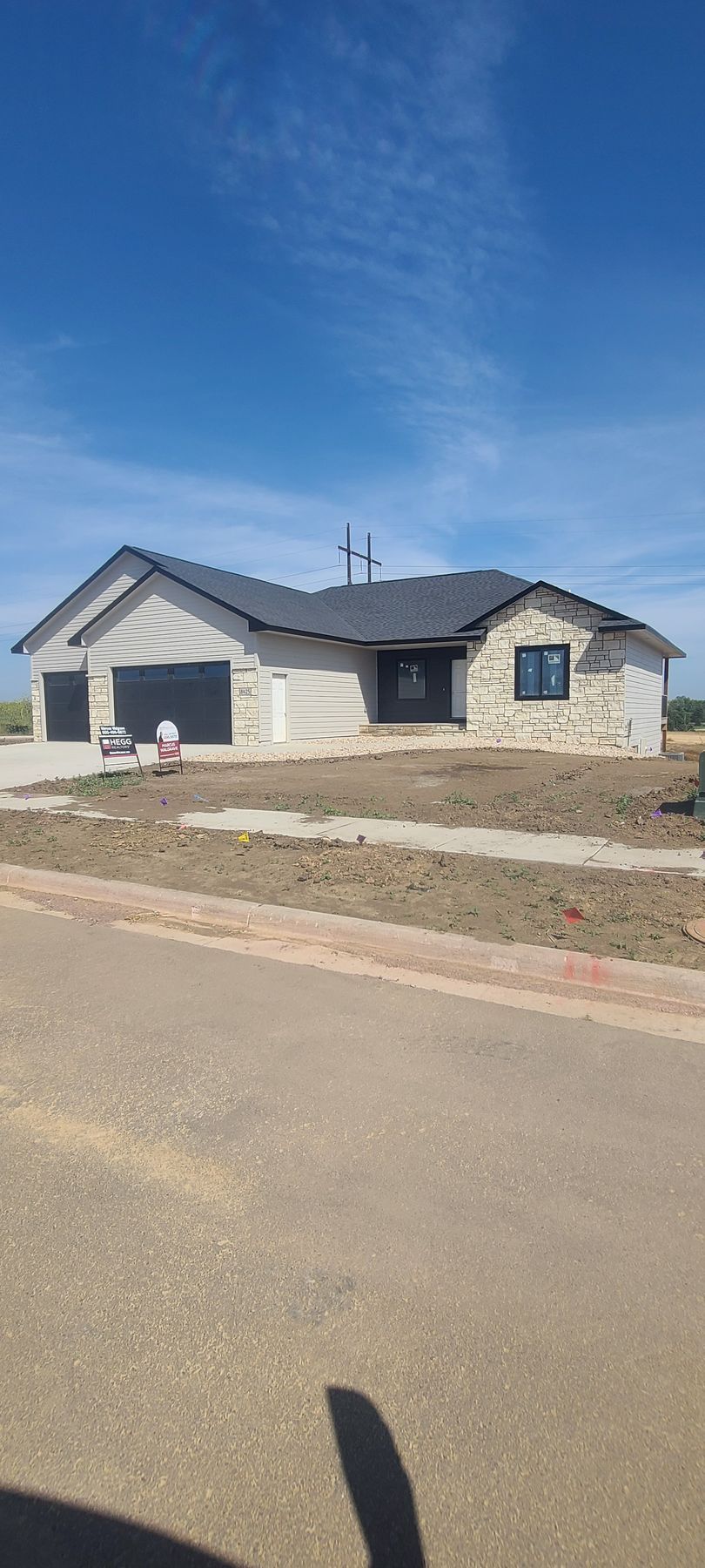 House under construction with stone facade, two-car garage, and dark roof under a blue sky.