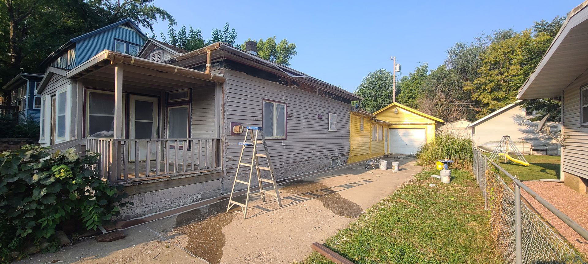 House with porch and garage; construction, ladder, and wet ground are visible.