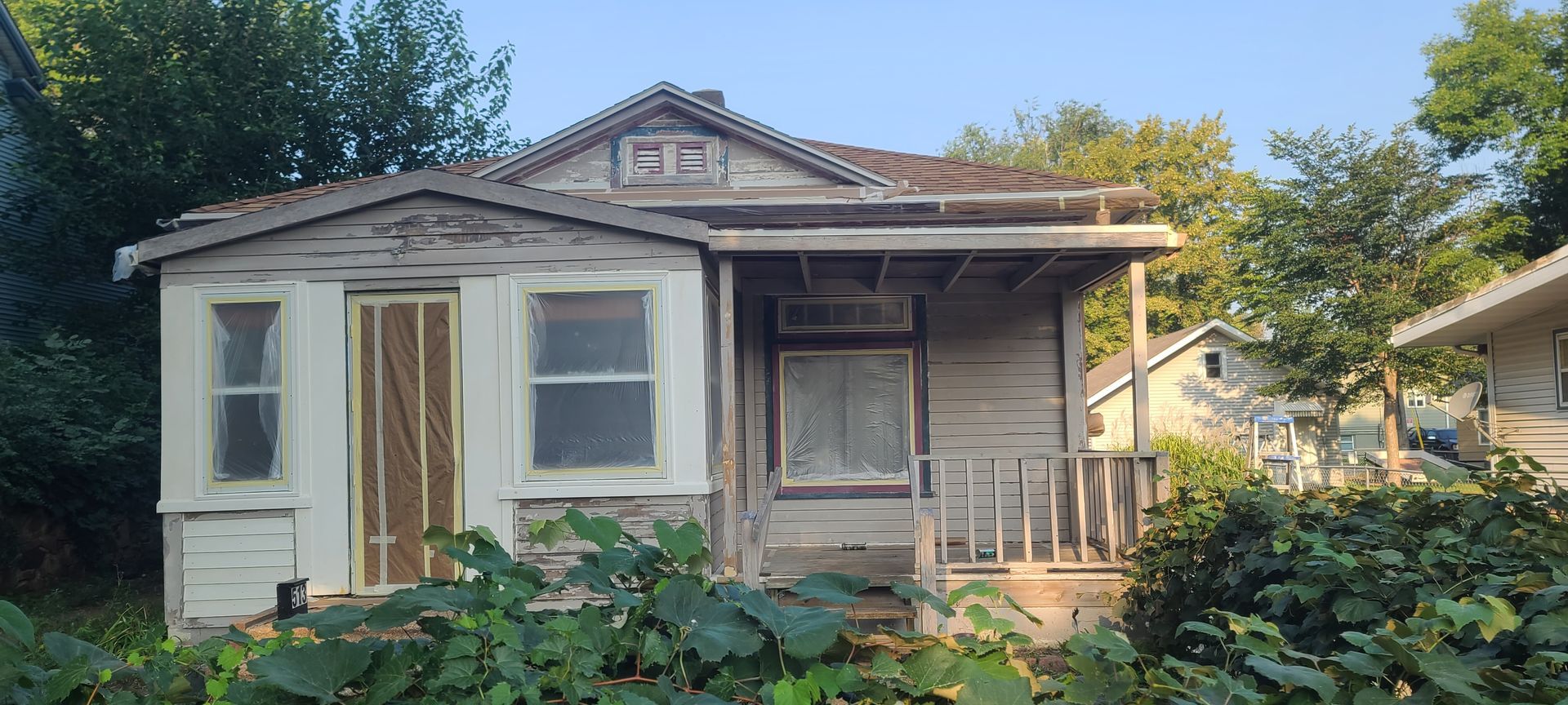 Dilapidated, single-story house with overgrown foliage, weathered wood, and a small porch.