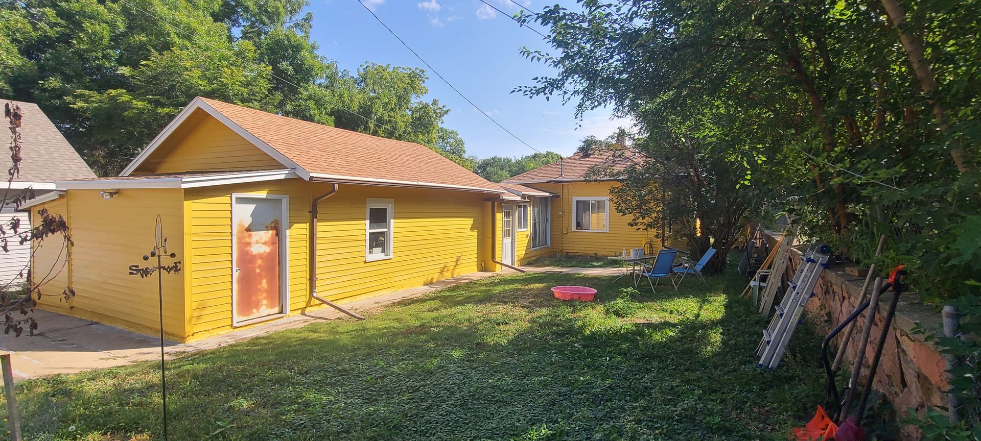 Yellow houses with brown roofs in a grassy yard, surrounded by trees. Blue sky visible.